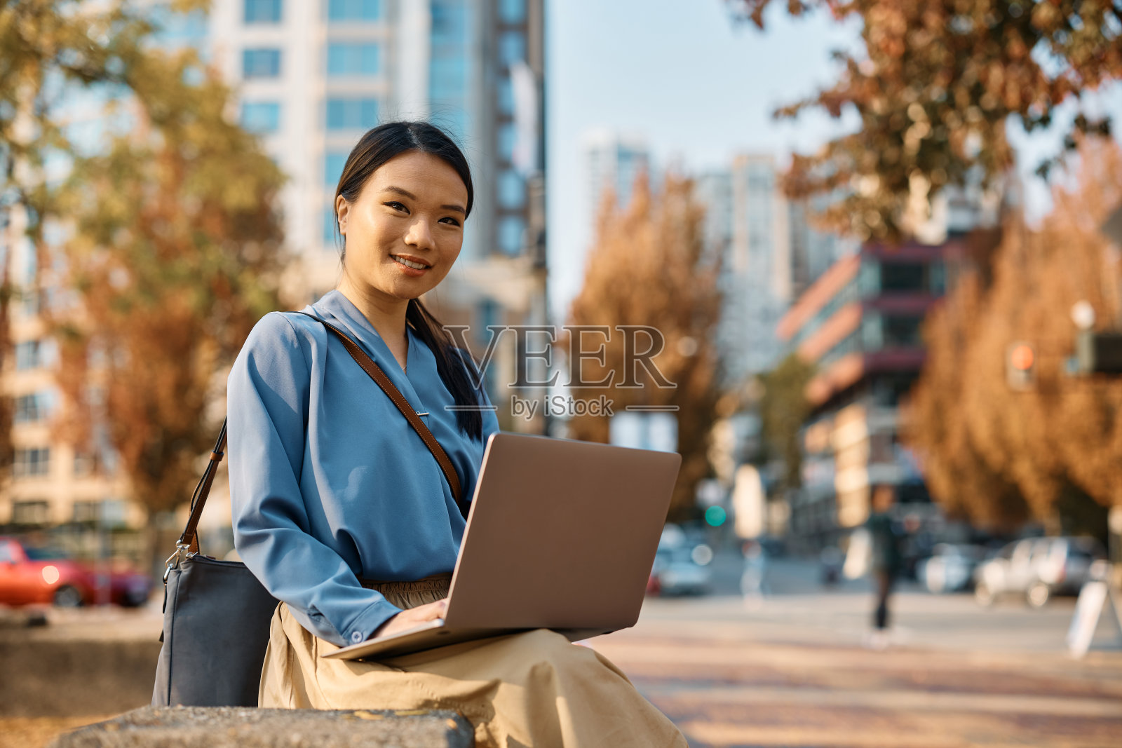 微笑的亚洲女性自由职业者使用笔记本电脑在公园和看着相机。照片摄影图片