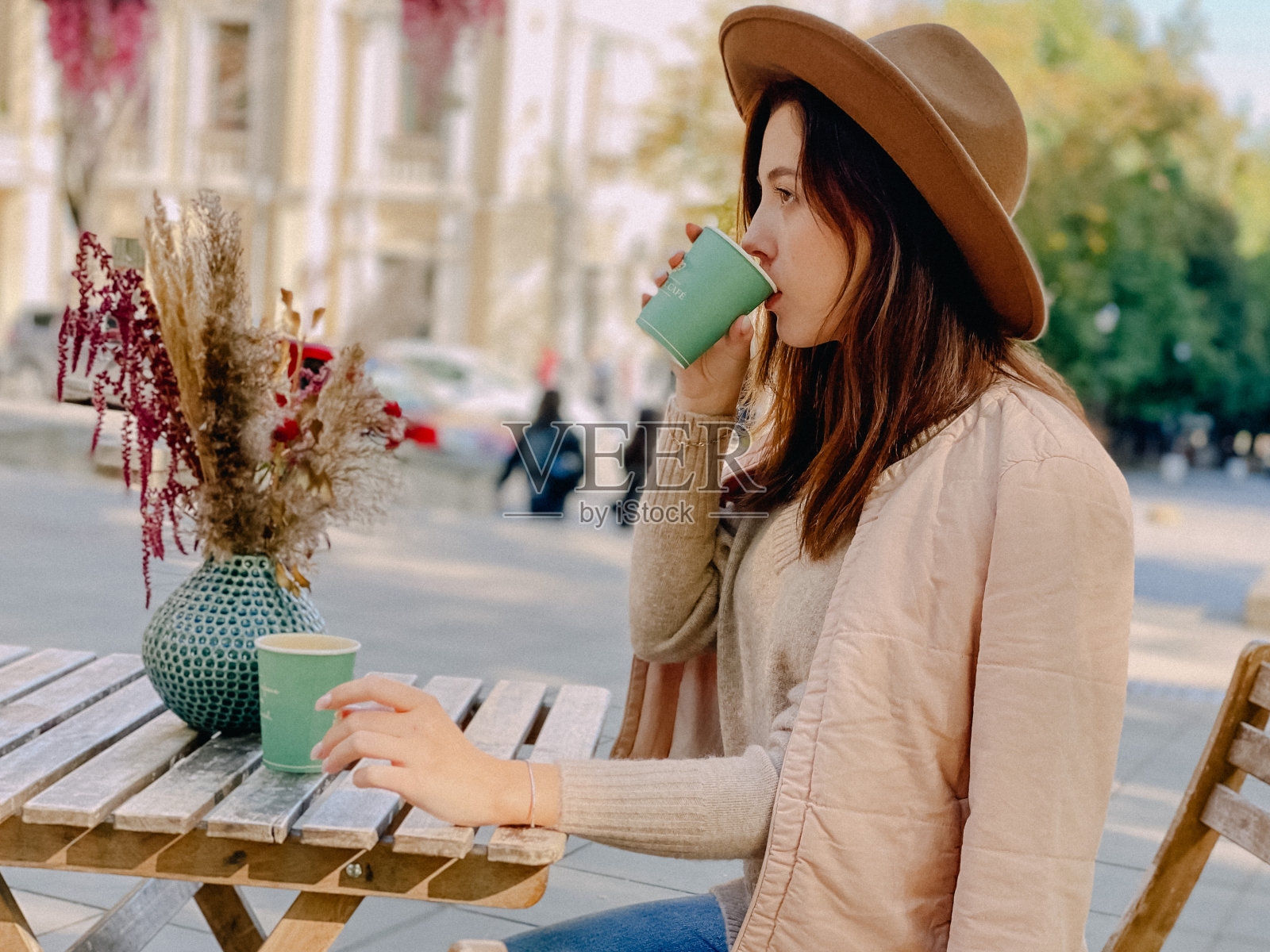 戴着米色帽子的年轻漂亮女子坐在外面的咖啡馆里喝着咖啡照片摄影图片