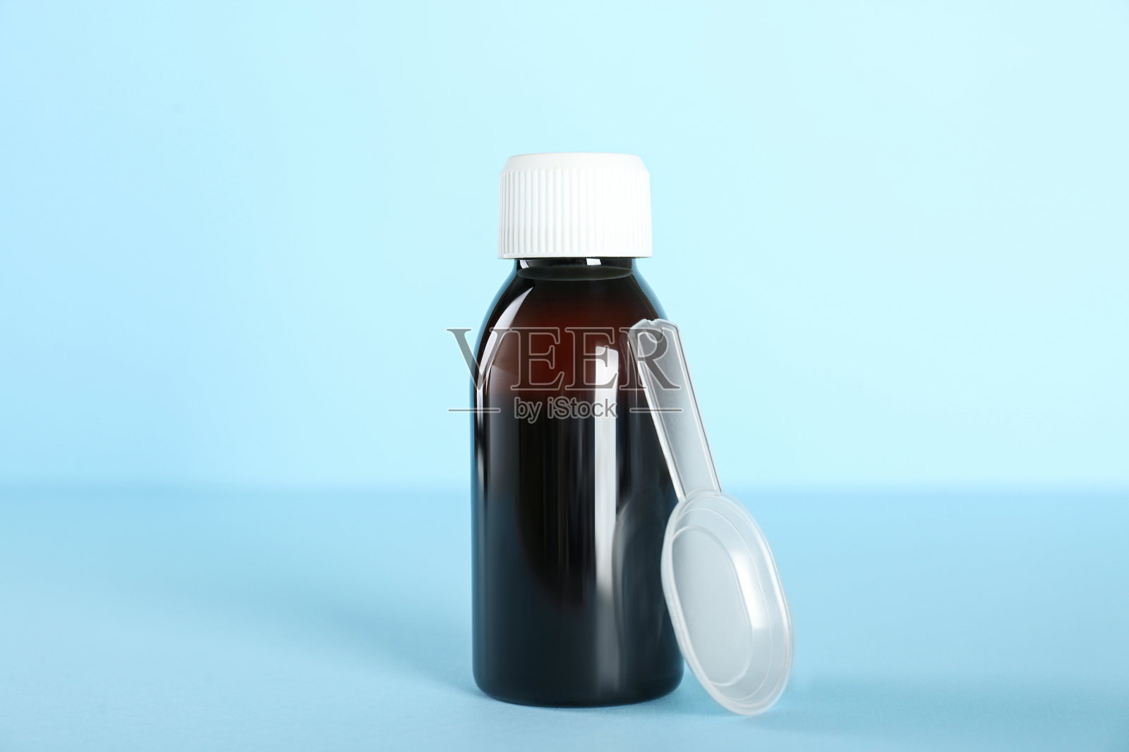 一瓶止咳糖浆和浅蓝色背景的给药勺照片摄影图片