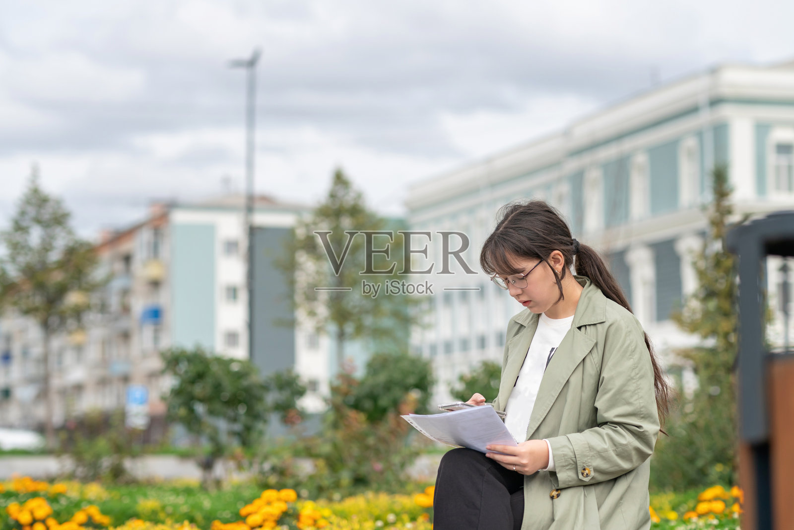 一个女孩坐在街上的长凳上,手里拿着文件,用着手机照片摄影图片