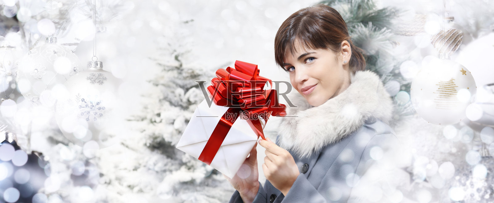 快乐的女人拿着快乐的圣诞礼物红盒子包装,孤立的背景与树和球模糊散景灯,促销购物的模板,广告横幅海报或礼品卡照片摄影图片
