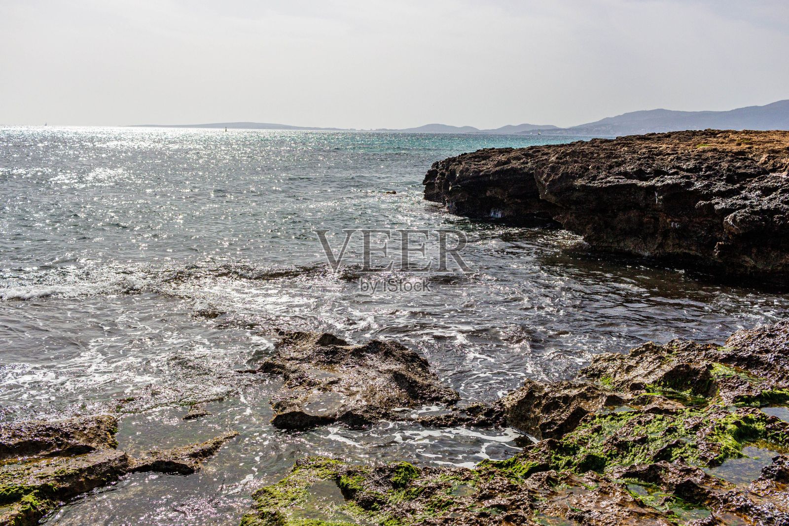 岩石海岸和灰蓝色的海,背景是小山。照片摄影图片