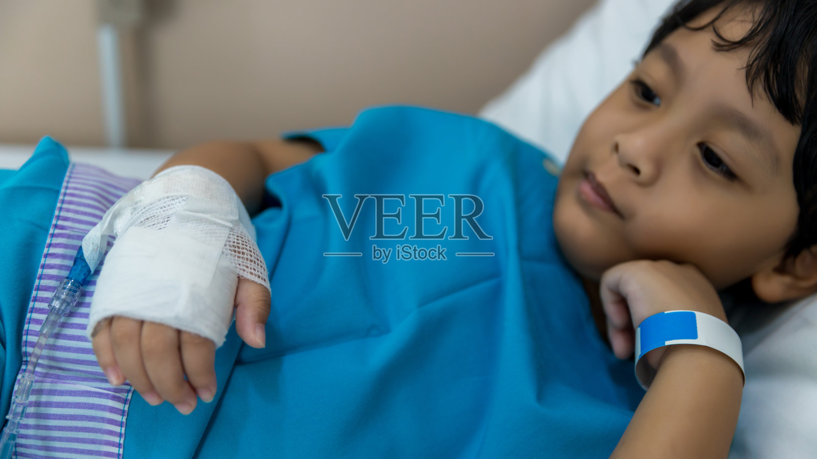 患儿的手上有盐水注射器。疾病和治疗。生病的男孩躺在医院的床上。照片摄影图片