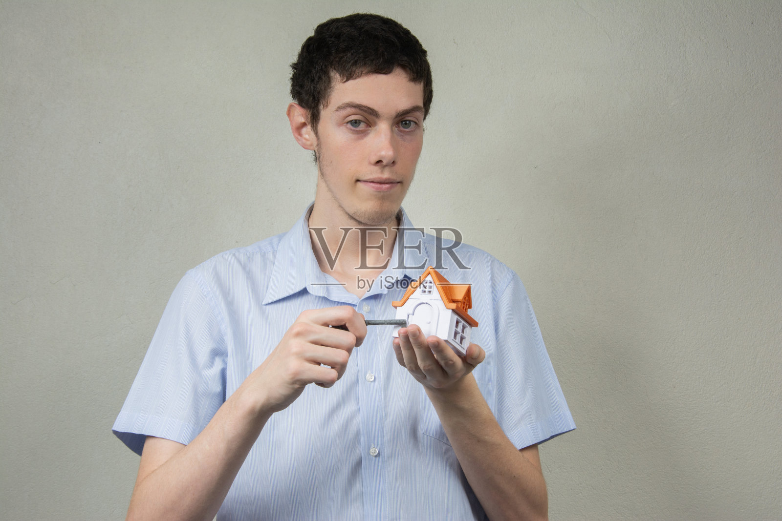 年轻人拿着一把钥匙和一座迷你房子照片摄影图片