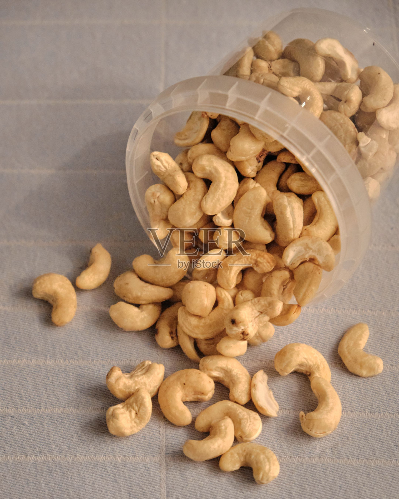 特写的腰果在一个塑料容器散落在桌布上照片摄影图片