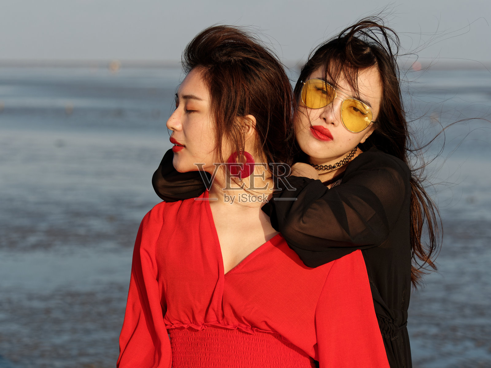 美丽的中国女孩穿着红黑相间的衣服,在阳光明媚的海滩上拥抱在一起。最好的年轻女孩朋友在夏天享受无忧无虑的时光,情感,人,美丽和生活方式的概念。照片摄影图片