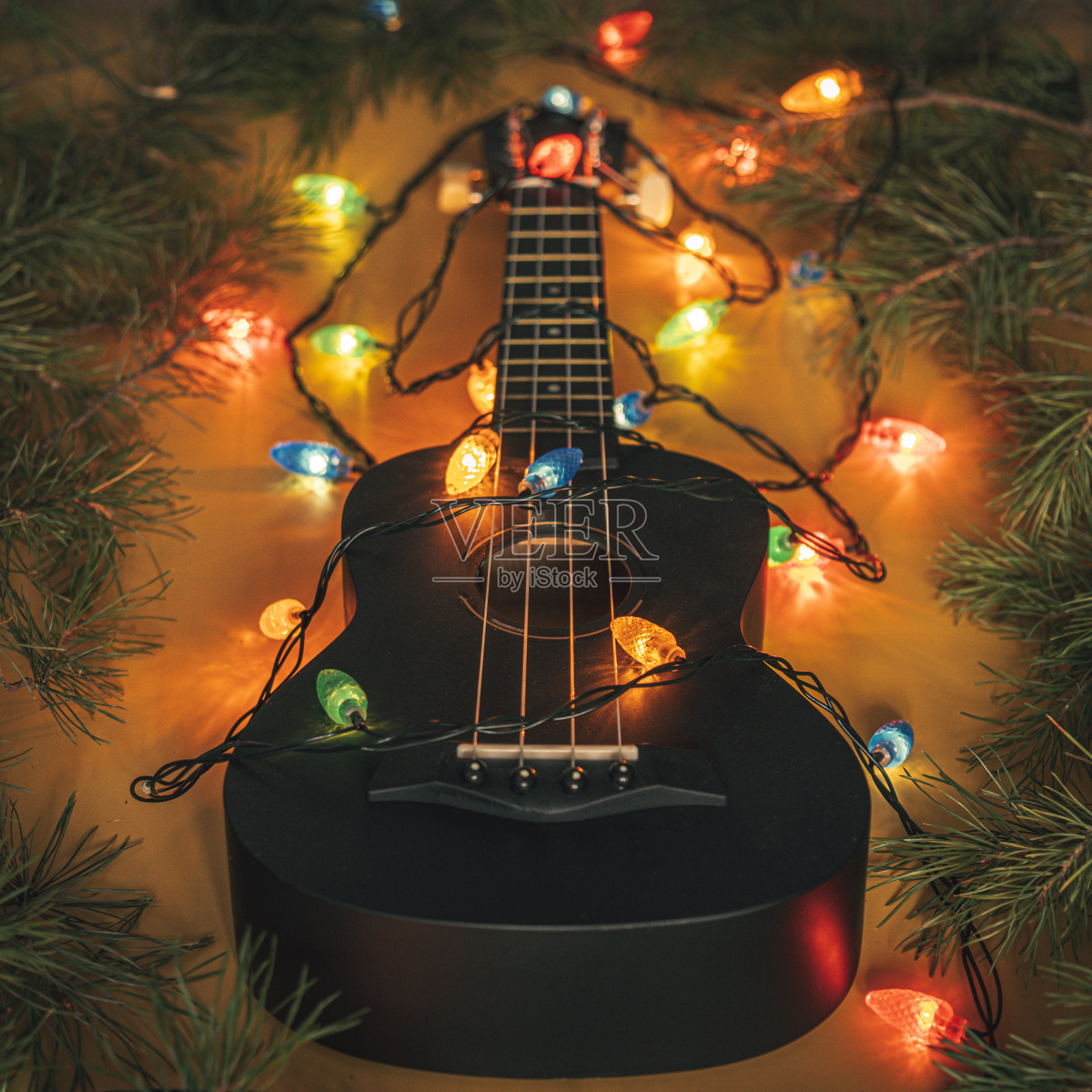 黑色的尤克里里吉他和圣诞装饰在黑暗的背景。夏威夷吉他与点燃的花环在黑暗的背景。新年和圣诞音乐,概念照片摄影图片