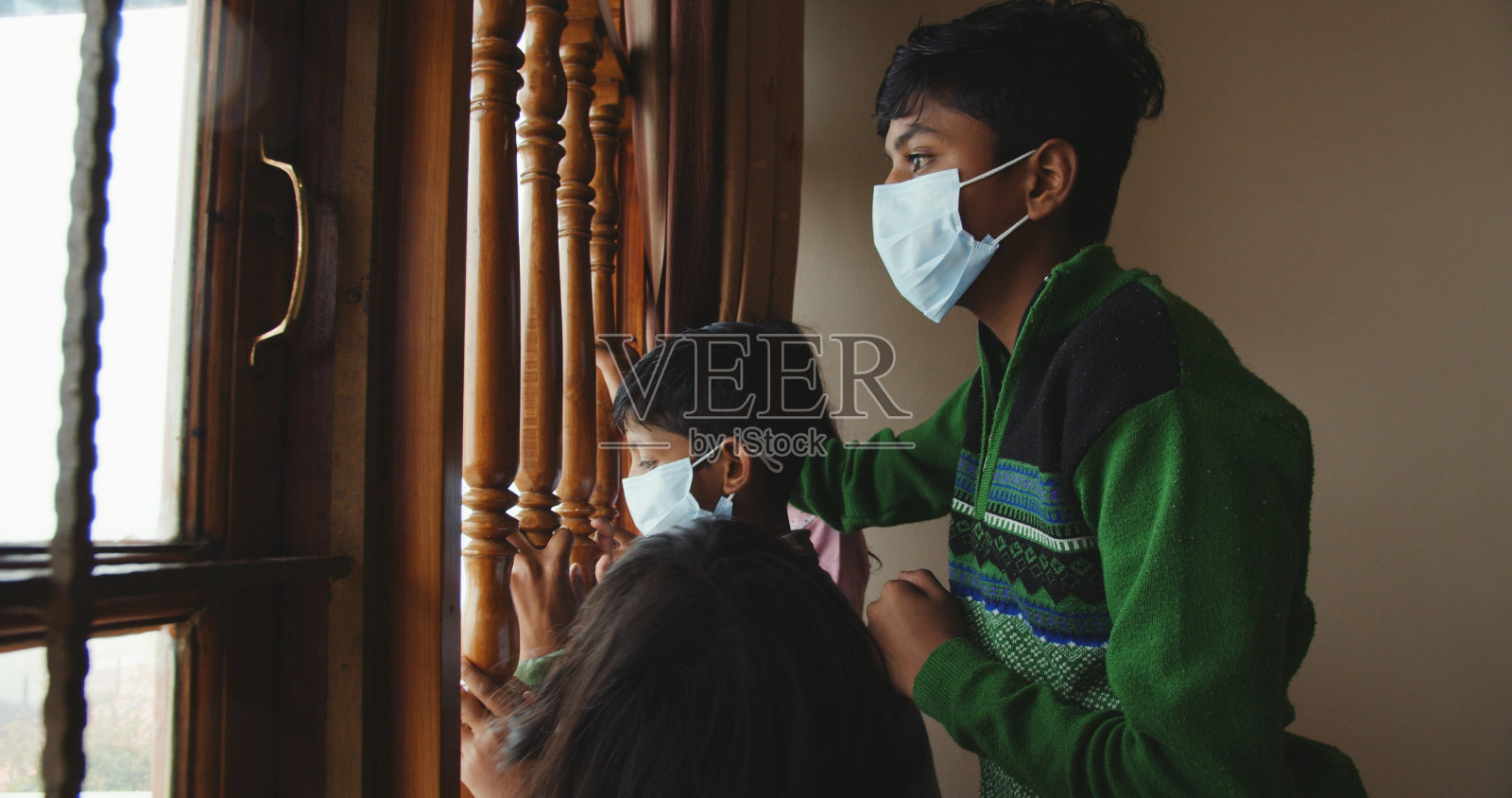 冠状病毒期间,来自印度的兄弟姐妹戴着口罩向窗外望去照片摄影图片