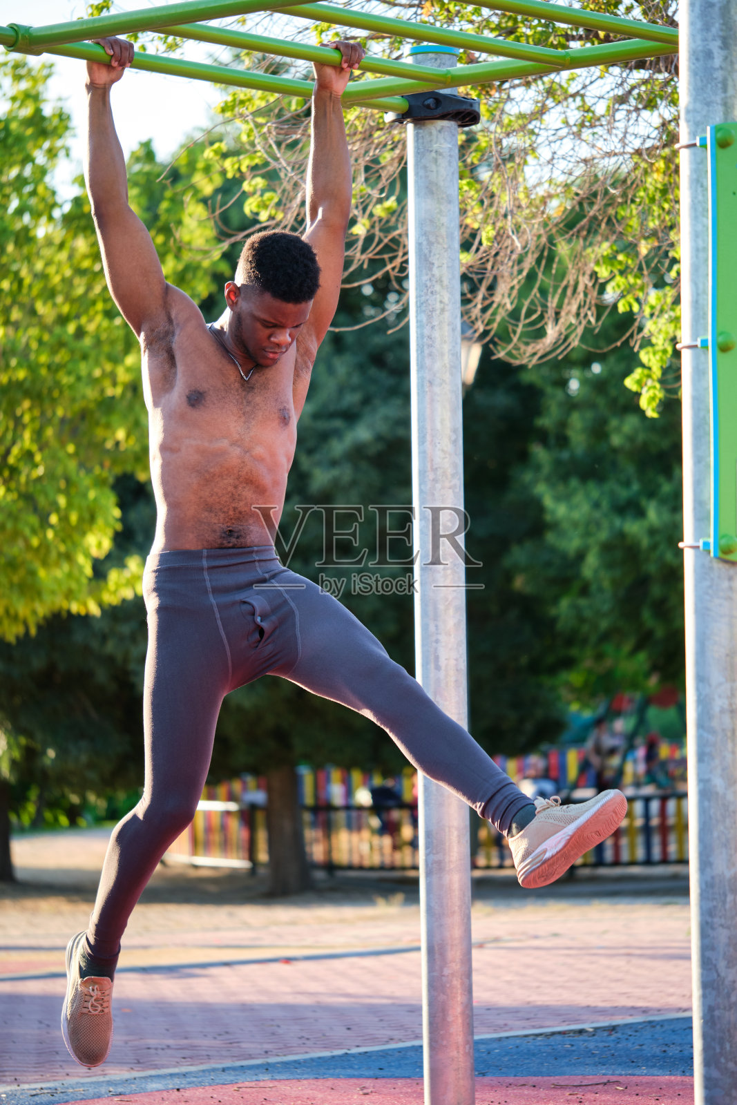 阳光明媚的日子,年轻健美的赤膊黑人男子在户外单杠上锻炼。照片摄影图片