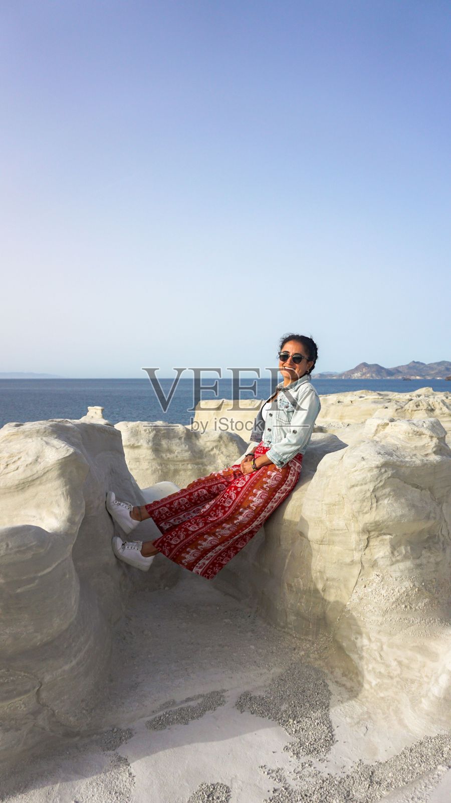 一个女人靠在白色岩石上的垂直镜头。地中海沿岸,希腊。照片摄影图片