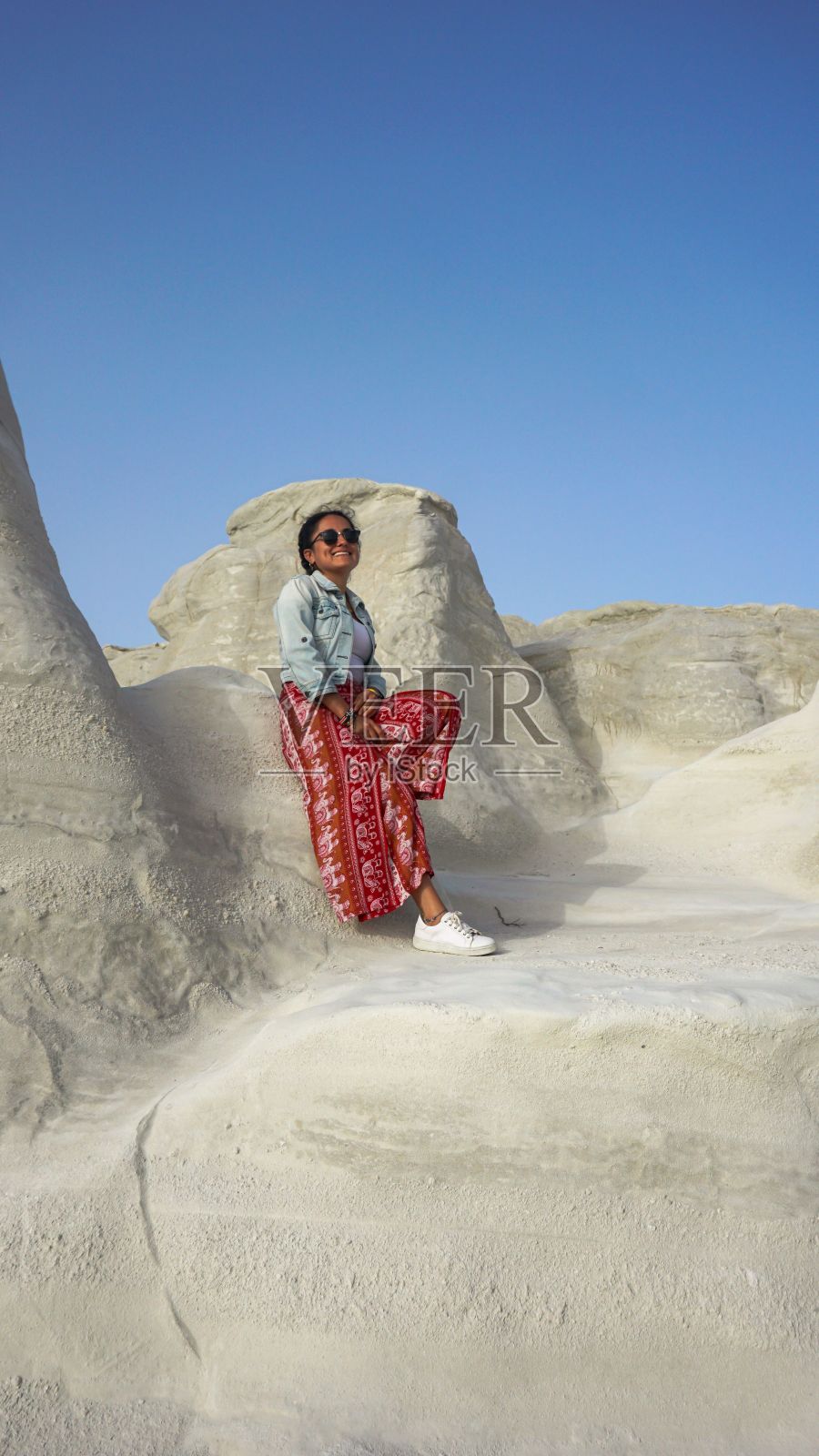 一个女人靠在白色岩石上的垂直镜头。地中海沿岸,希腊。照片摄影图片