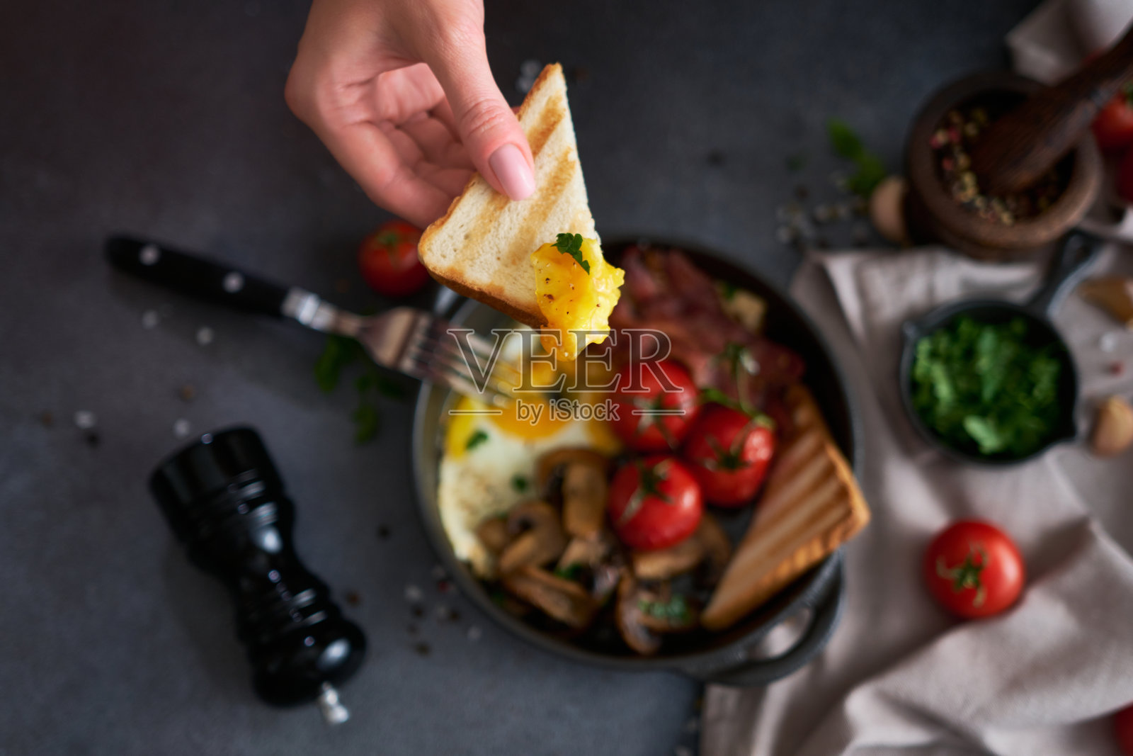 在家庭厨房用黑色陶瓷锅煎蛋、培根、番茄和烤面包照片摄影图片