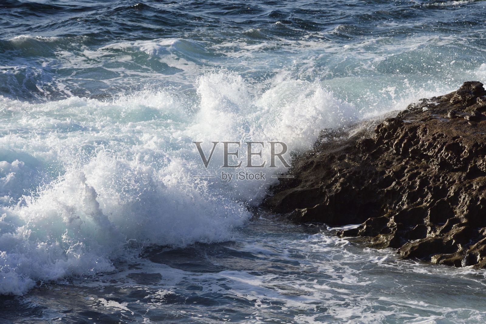 特写阳光下的水波击中不均匀的海滩石头产生泡沫照片摄影图片