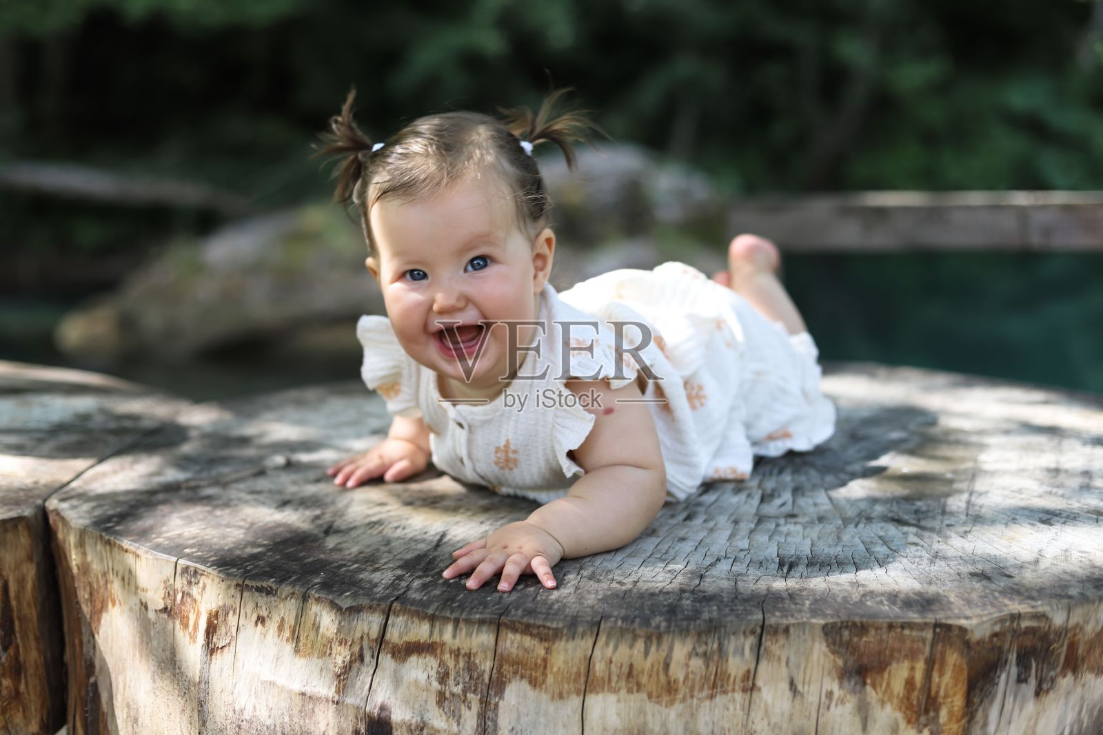 一个可爱的女婴在树干上涂鸦,后面有树和一条河照片摄影图片