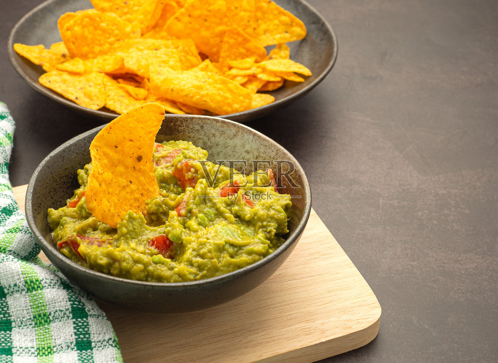 新鲜的鳄梨酱放在木砧板上,墨西哥玉米片放在盘子上照片摄影图片