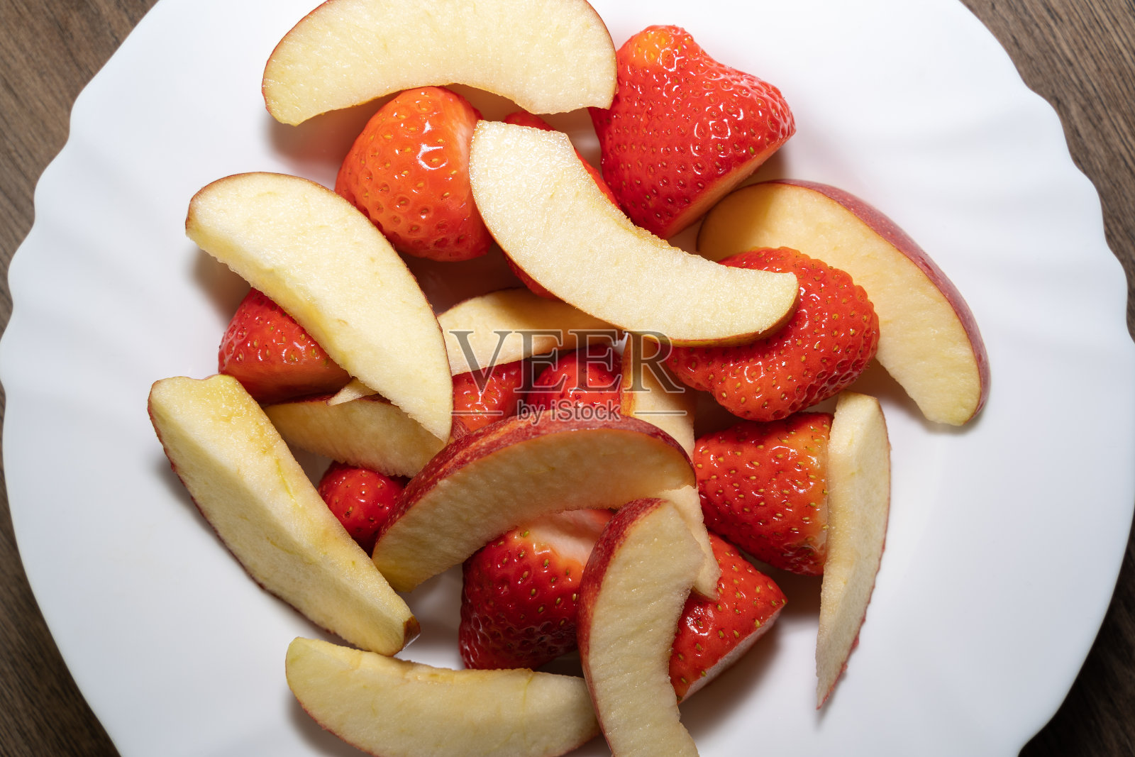 White plate with sliced apple pieces and strawberries照片摄影图片