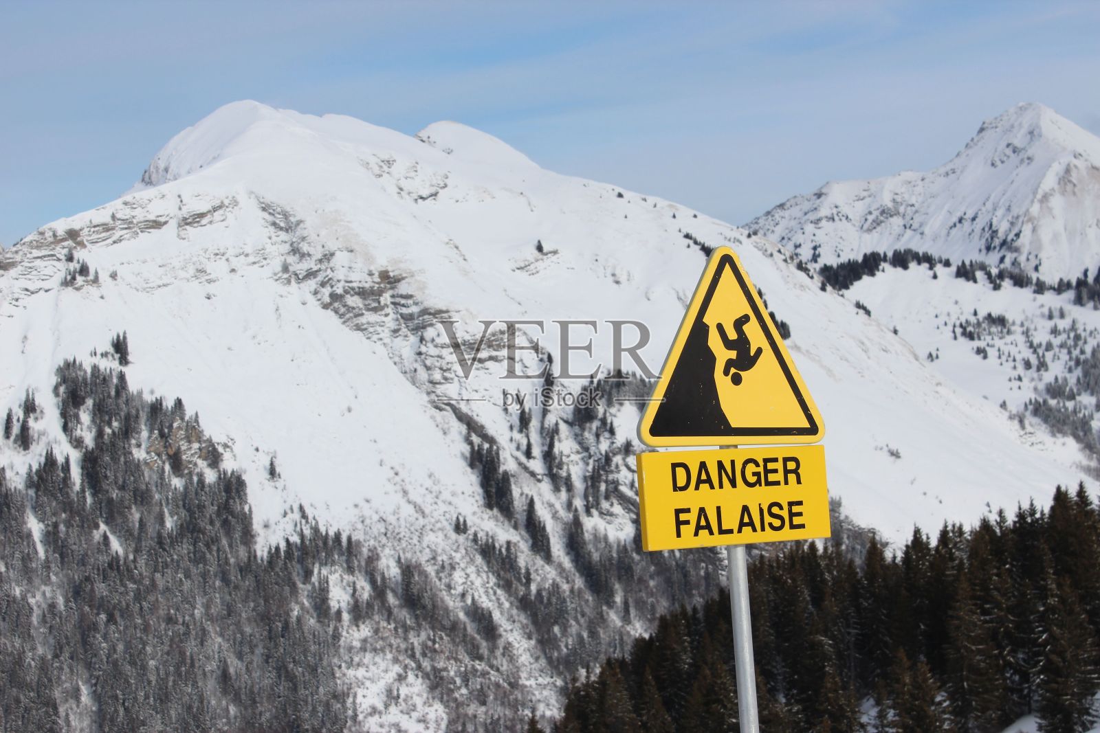 在冬天,一个被松树和积雪覆盖的山脉中,一个“危险”标志的特写照片摄影图片