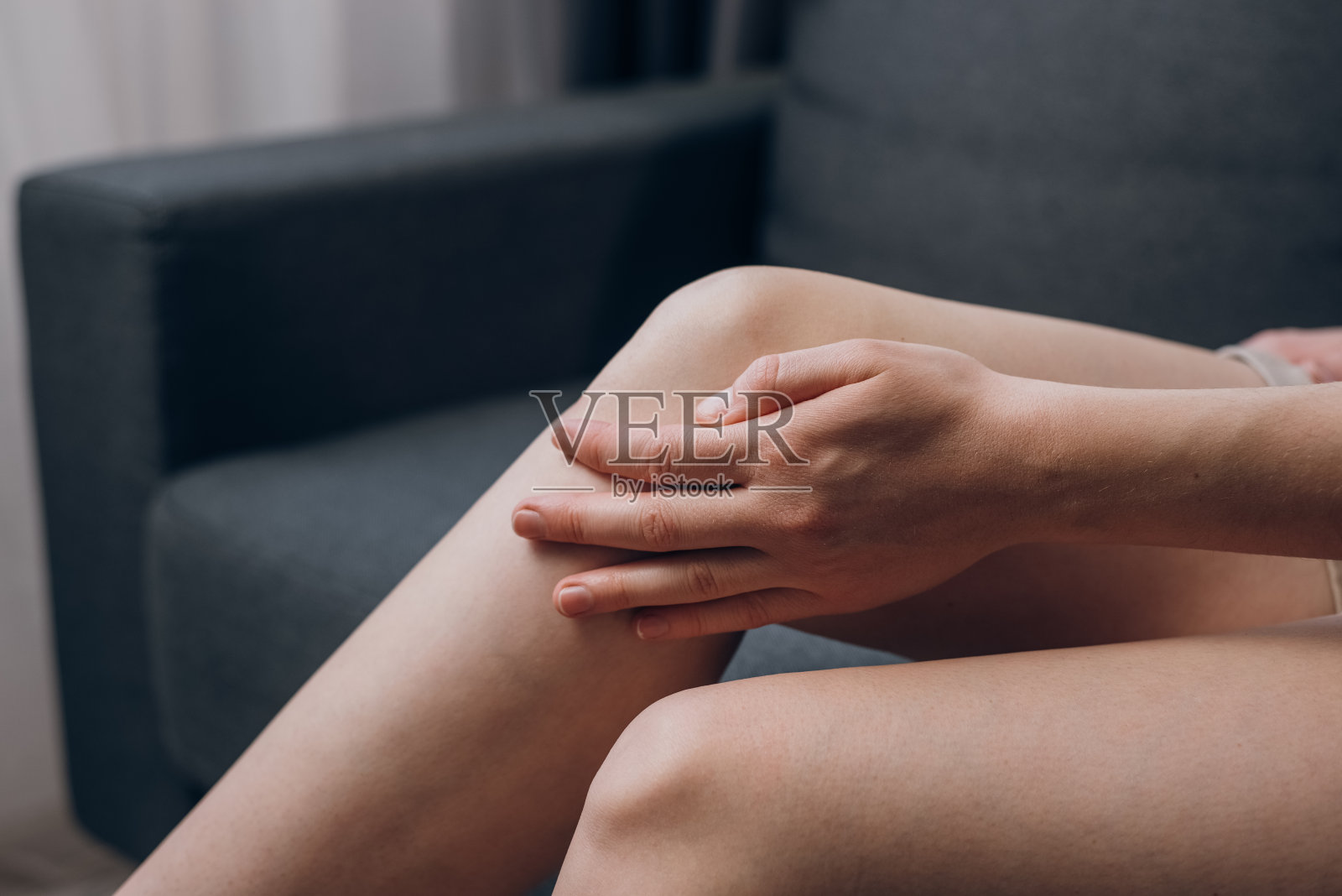 不健康的年轻女子坐在沙发上,感觉膝盖疼痛,在家里做按摩膝盖。女性腿部有半月板损伤或慢性关节炎症。保健和医疗概念照片摄影图片