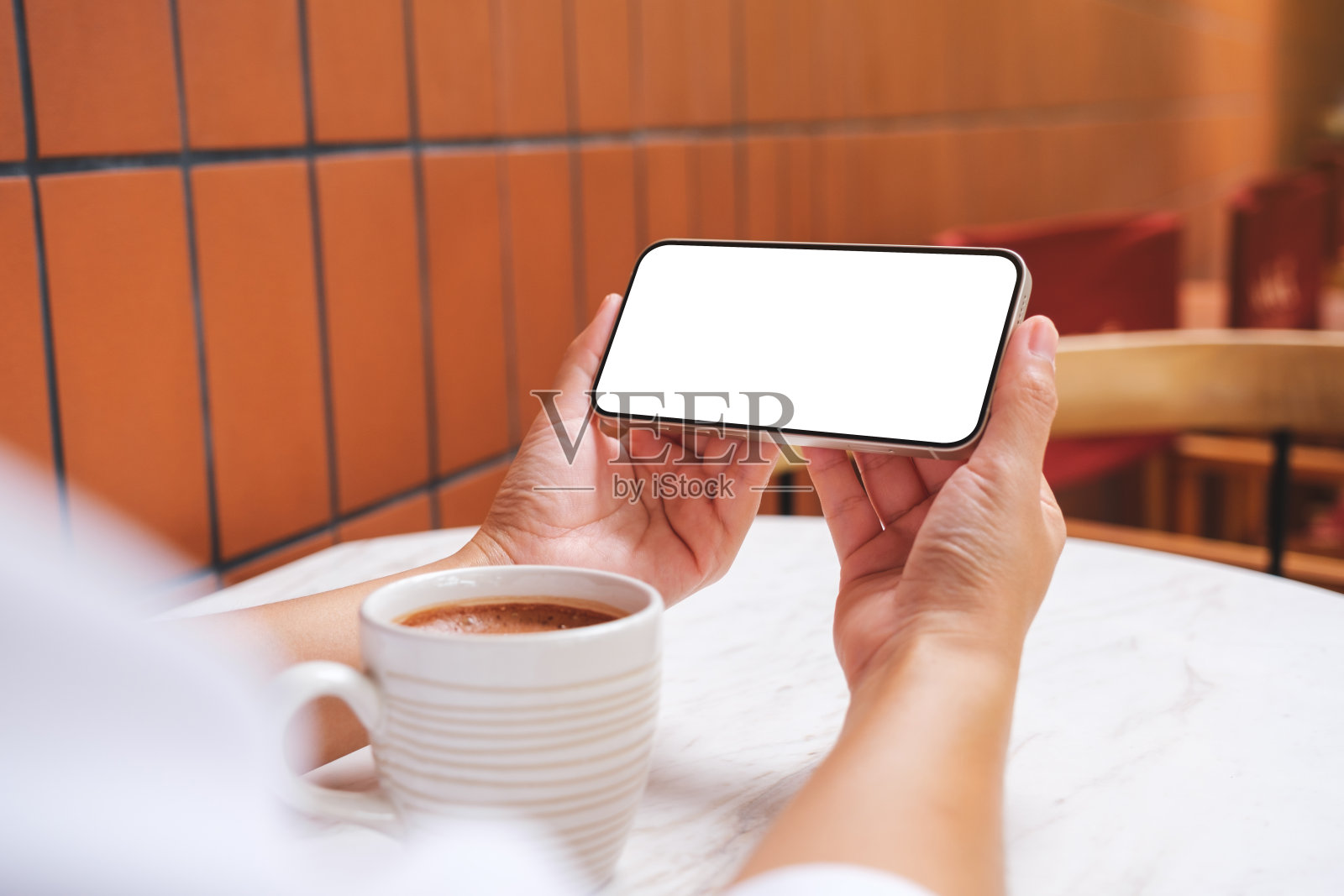 一个女人拿着空白桌面屏幕的手机,咖啡杯放在桌子上的模型图像照片摄影图片