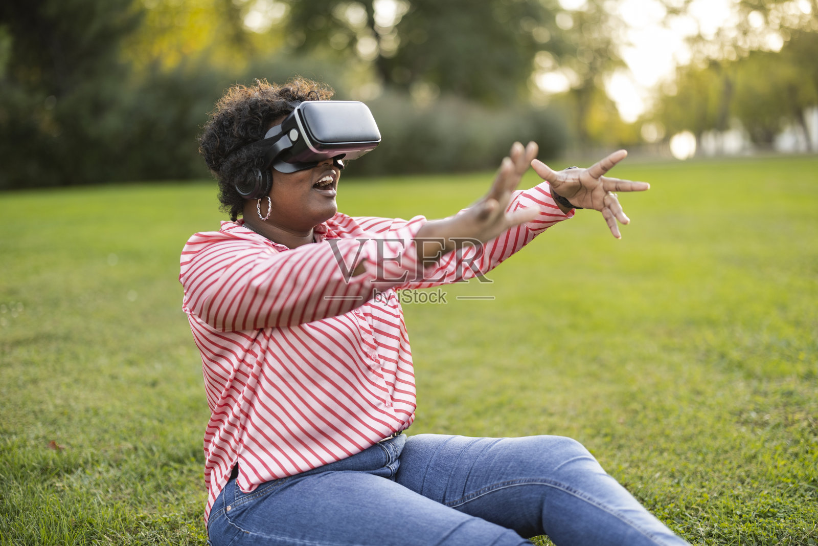 一名非裔美国女性坐在公园的草地上玩虚拟现实眼镜照片摄影图片