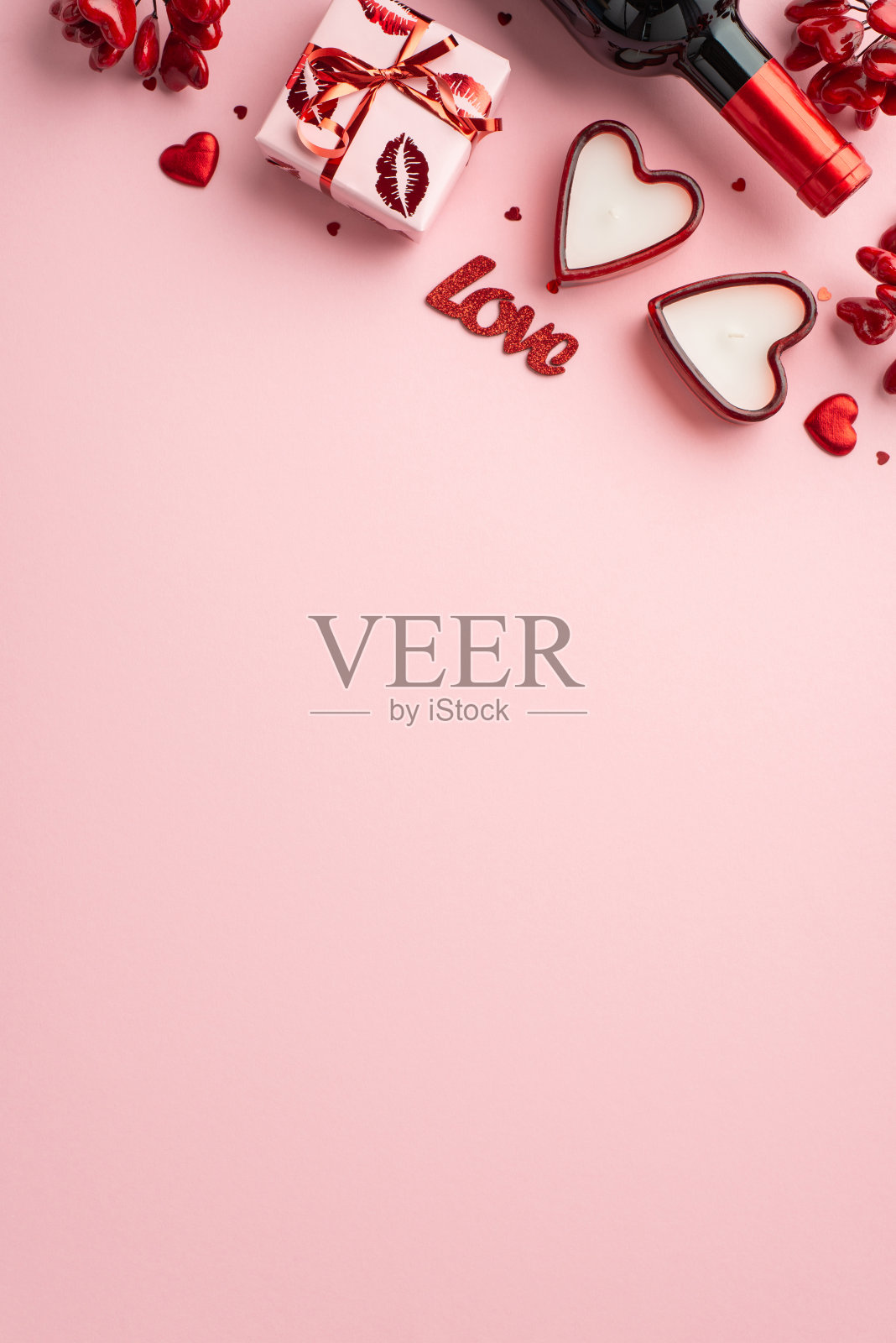 情人节的概念。俯视图小礼盒在包装与亲吻嘴唇图案酒瓶心形蜡烛和纸屑孤立的浅粉色背景与复制空间垂直照片照片摄影图片