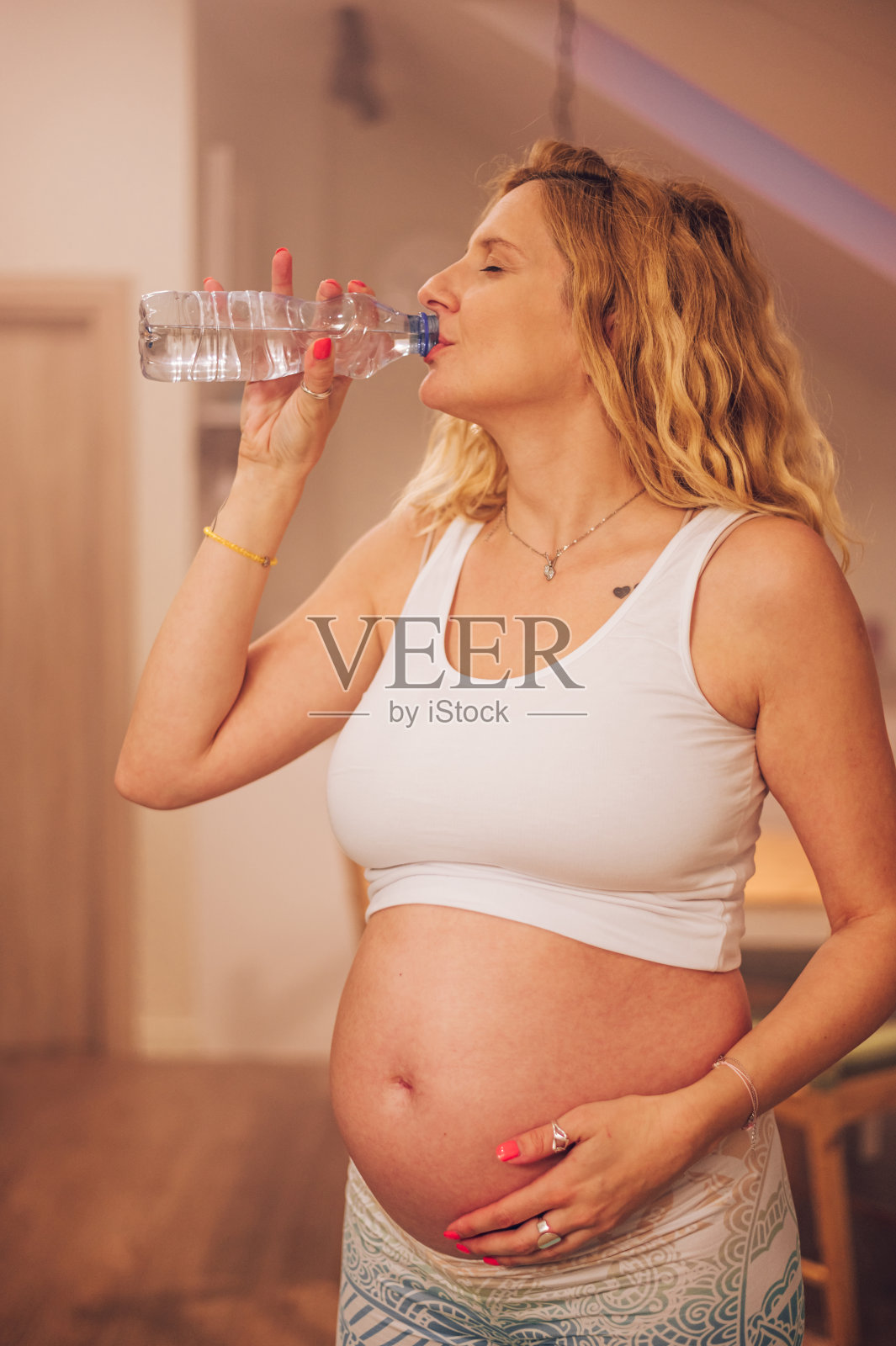 年轻孕妇在家做产前瑜伽,喝一瓶水照片摄影图片