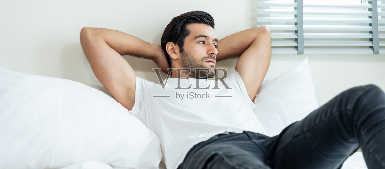 白人帅哥早上快乐地躺在床上。有吸引力的年轻性感男性感觉快乐和放松后从卧室的睡眠醒来,享受周末的休闲活动在房子里。照片摄影图片