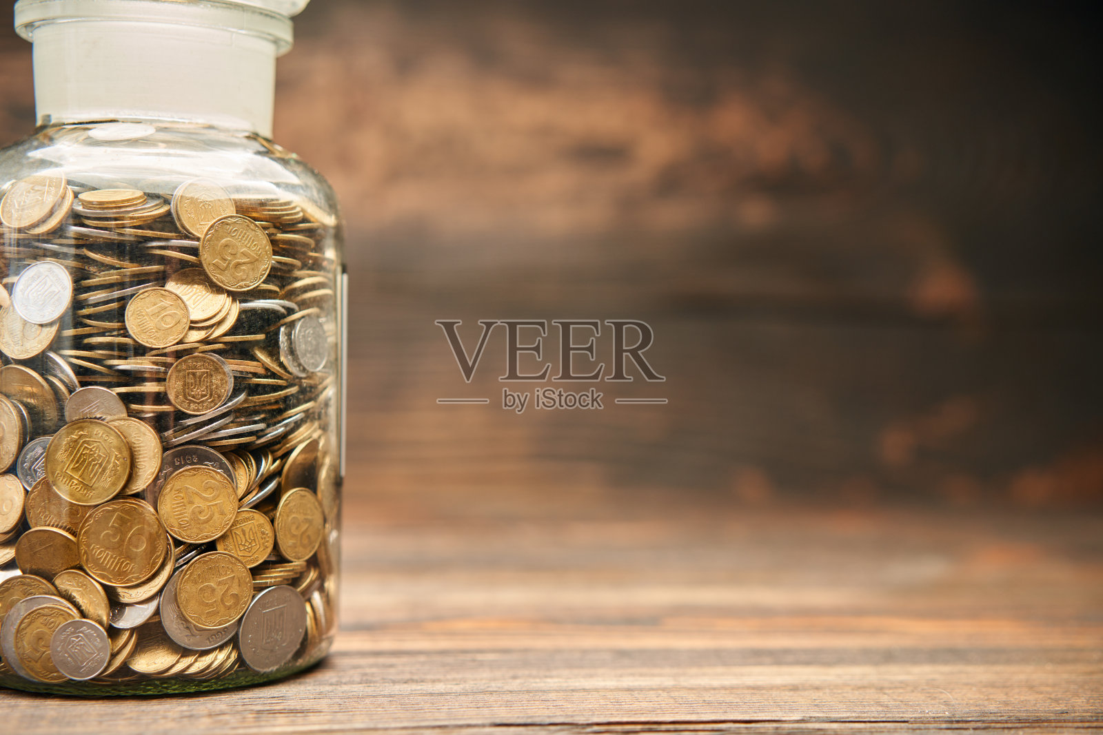 装满金币的玻璃罐子,木制背景上有文字复制空间。照片摄影图片