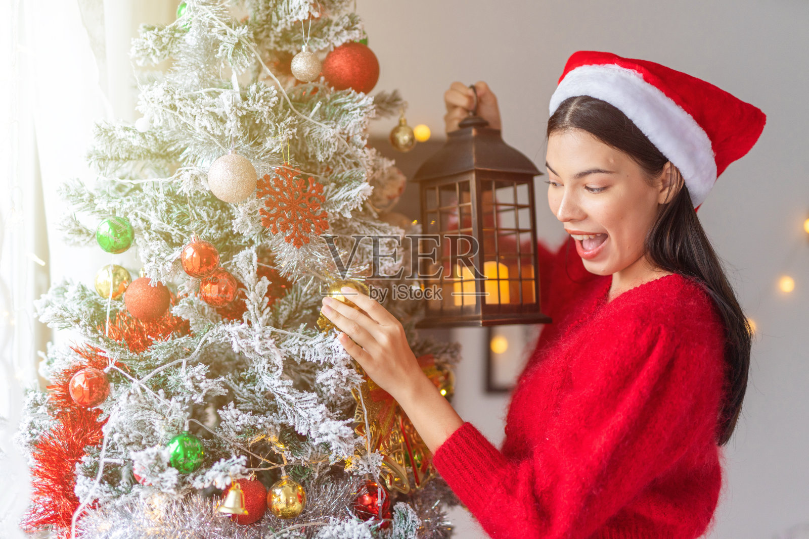 肖像照片的年轻美丽友好的亚洲女性女士与圣诞老人帽手持户外灯笼烛光旁边一个漂亮的装饰圣诞树照片摄影图片