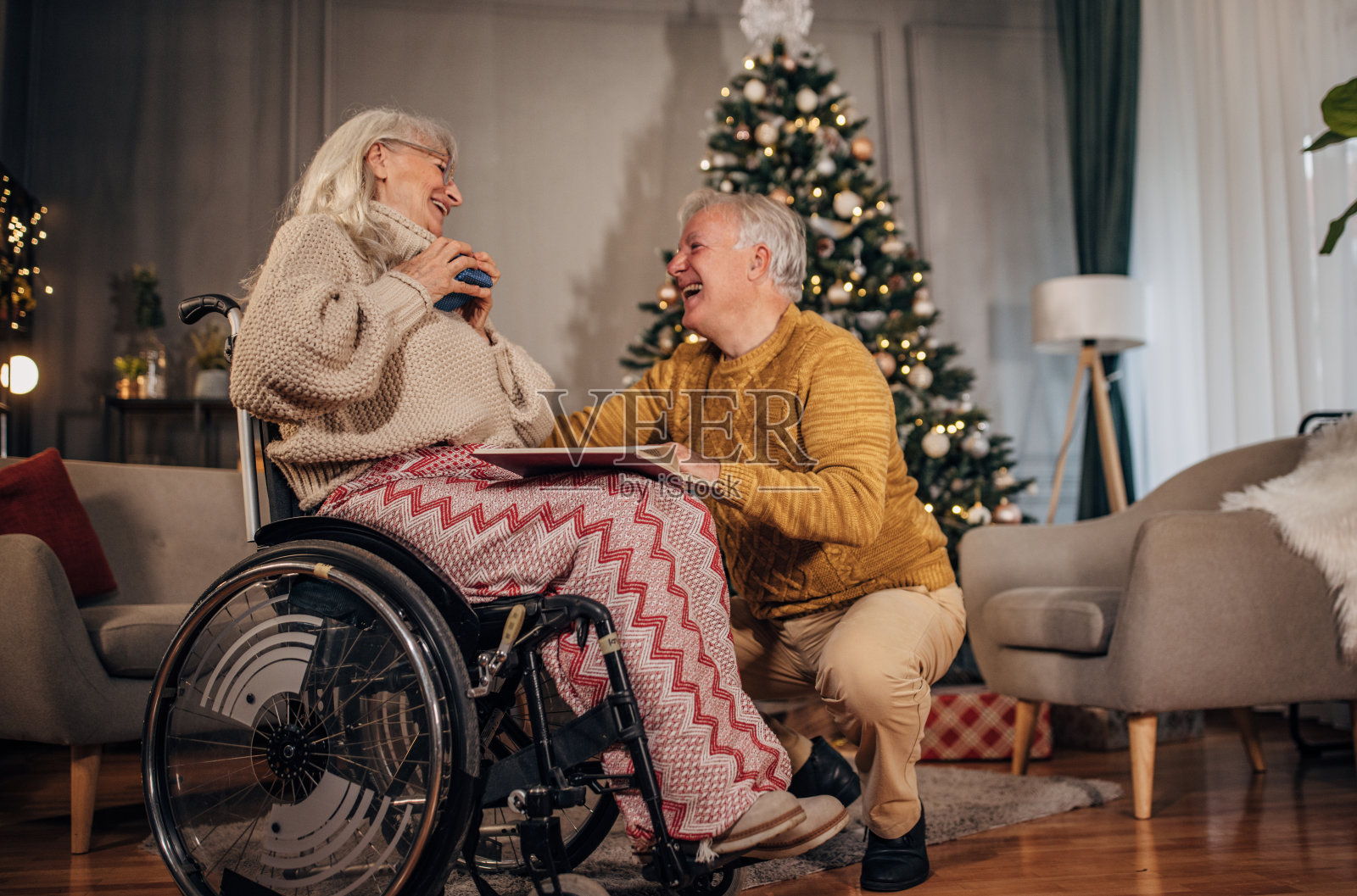 圣诞节那天,丈夫在家里用礼物给坐在轮椅上的妻子一个惊喜照片摄影图片