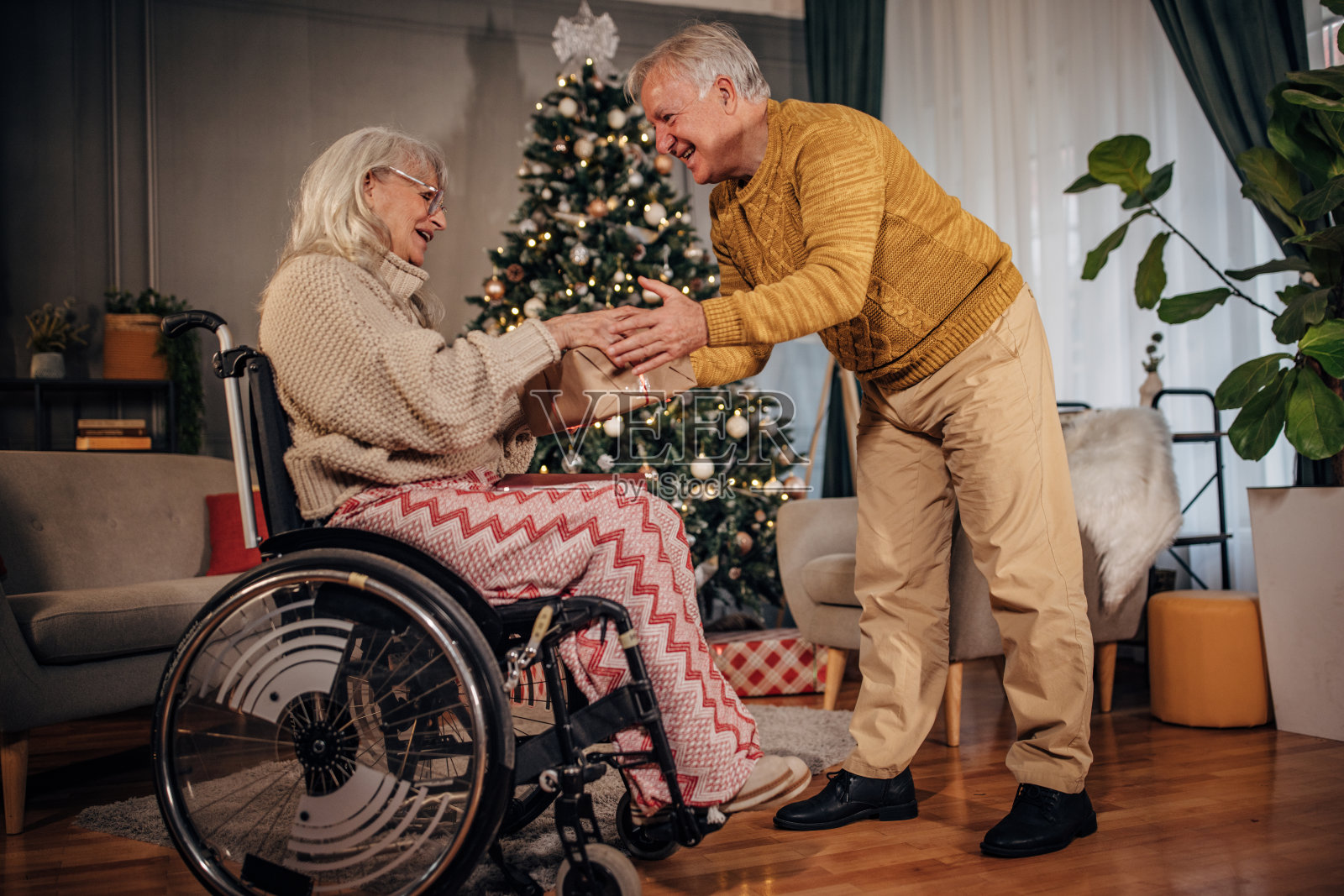 圣诞节那天,丈夫在家里用礼物给坐在轮椅上的妻子一个惊喜照片摄影图片