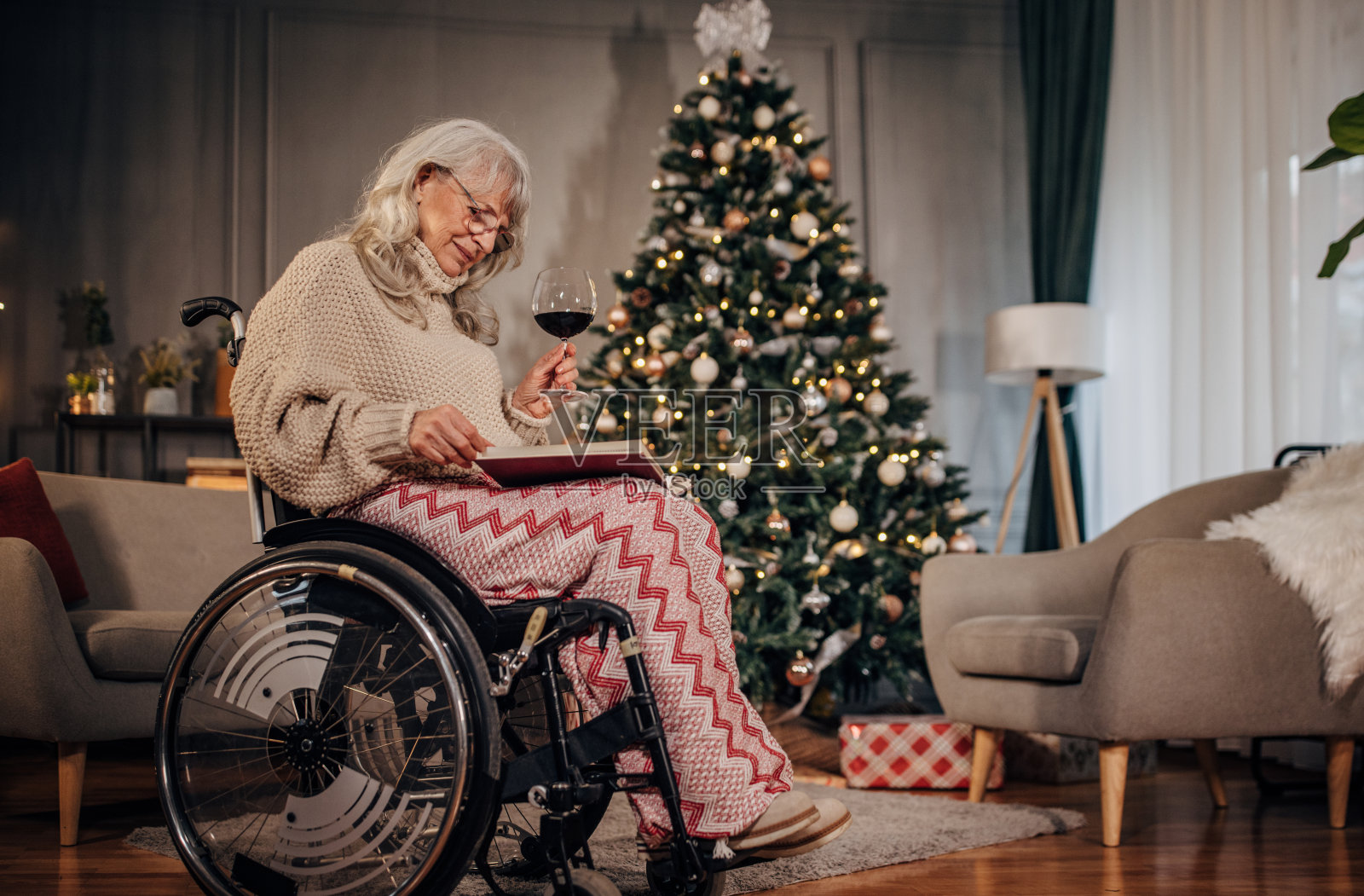 圣诞老人坐在轮椅上喝酒,看着相册照片摄影图片