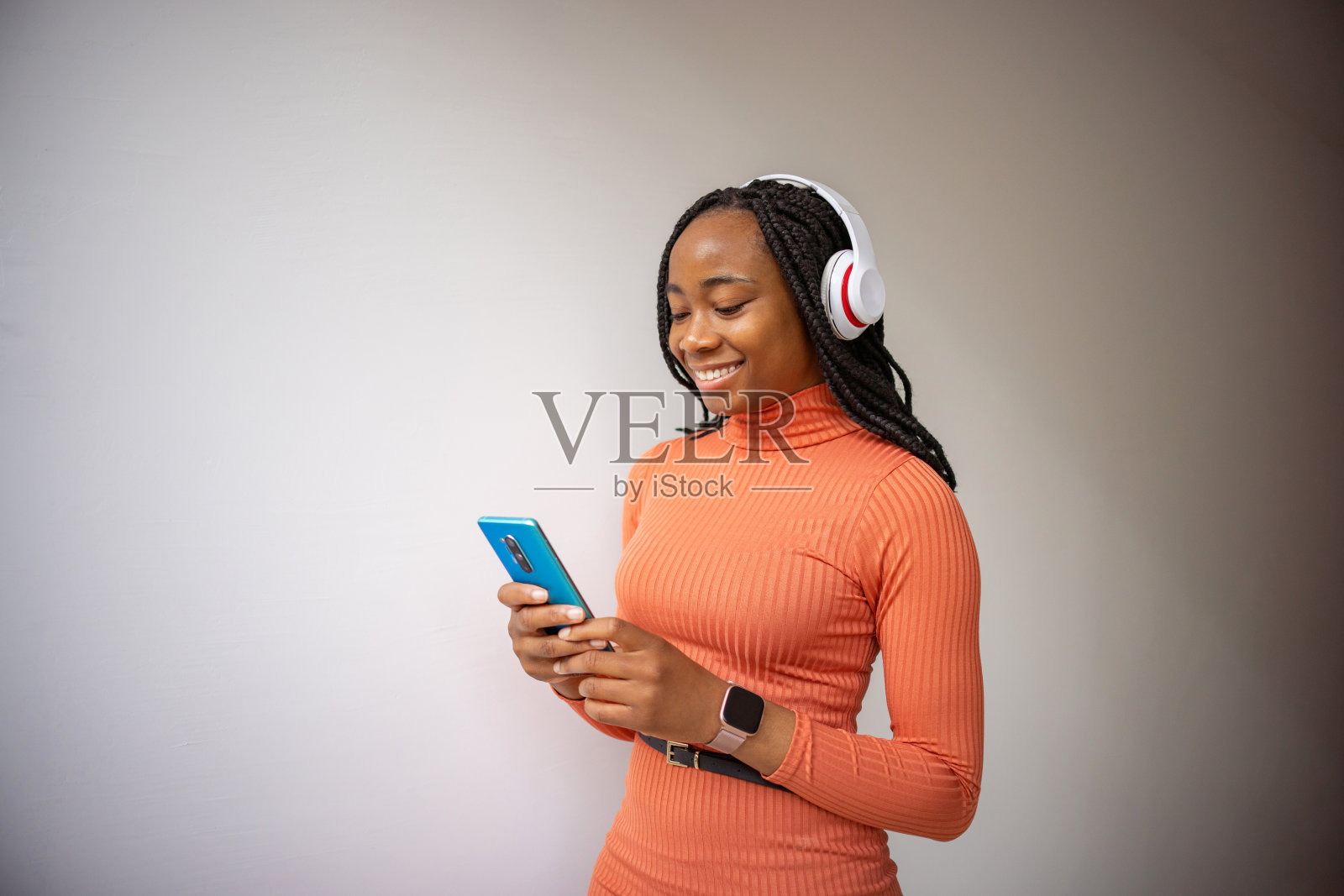 黑人妇女,穿着橙色衣服,戴着无线耳机,用手机照片摄影图片