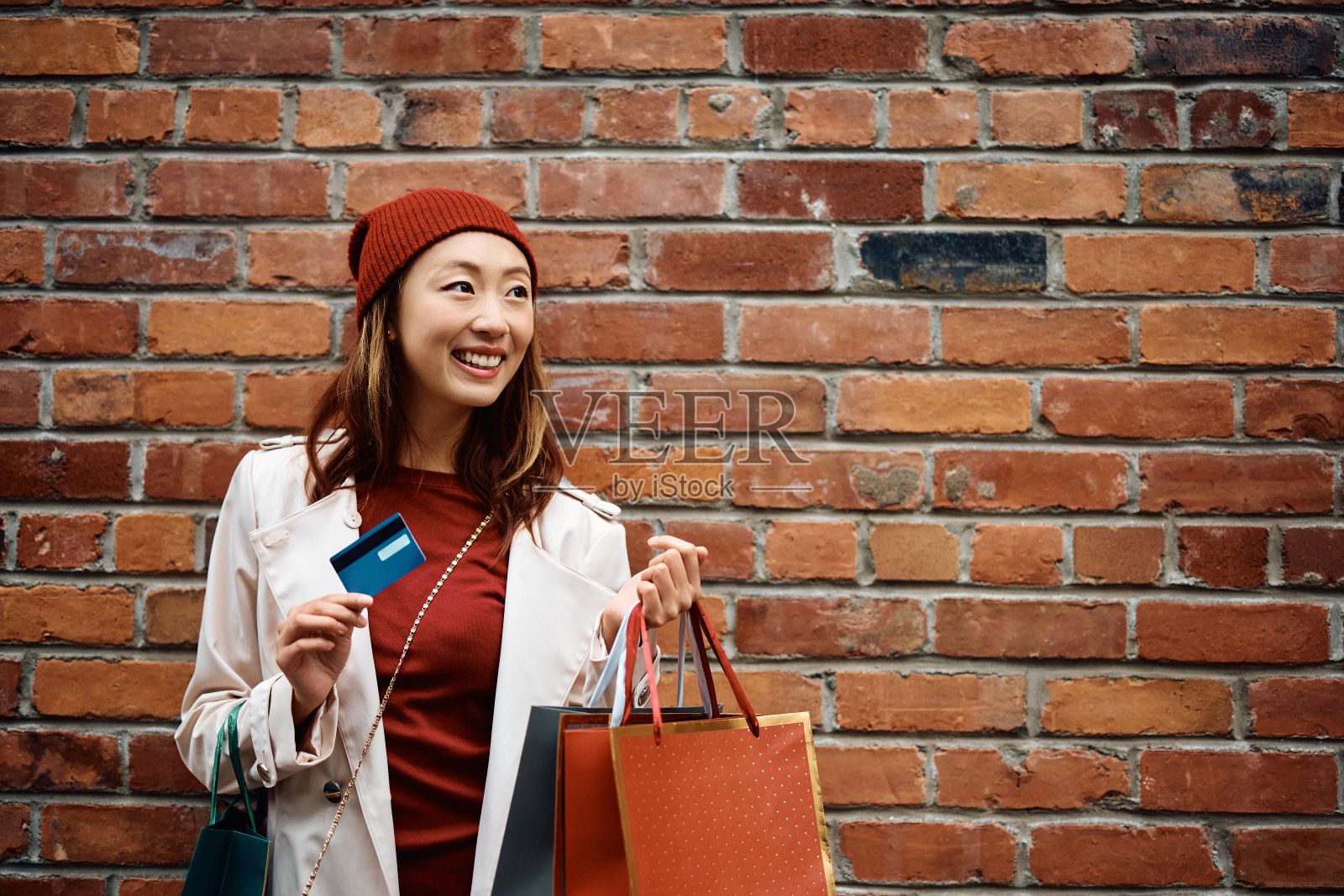 快乐的亚洲女人,信用卡和购物袋靠墙。照片摄影图片