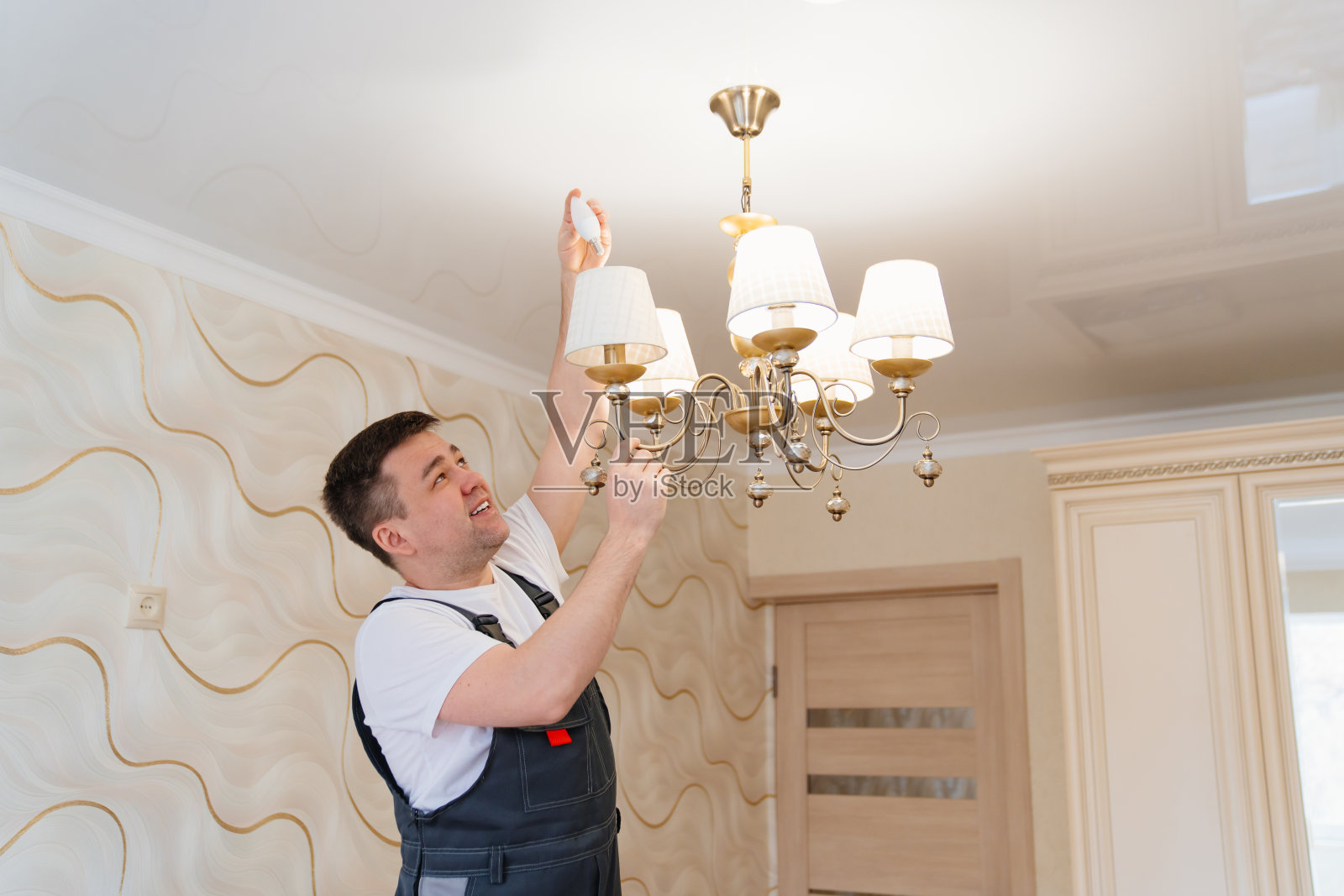 一位男电工正在更换吸顶灯上的灯泡。照片摄影图片