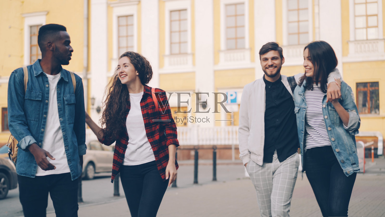 夏日里,游客朋友们穿着休闲服,背着背包,有说有笑地走在城市里。友谊,青年旅游理念。照片摄影图片