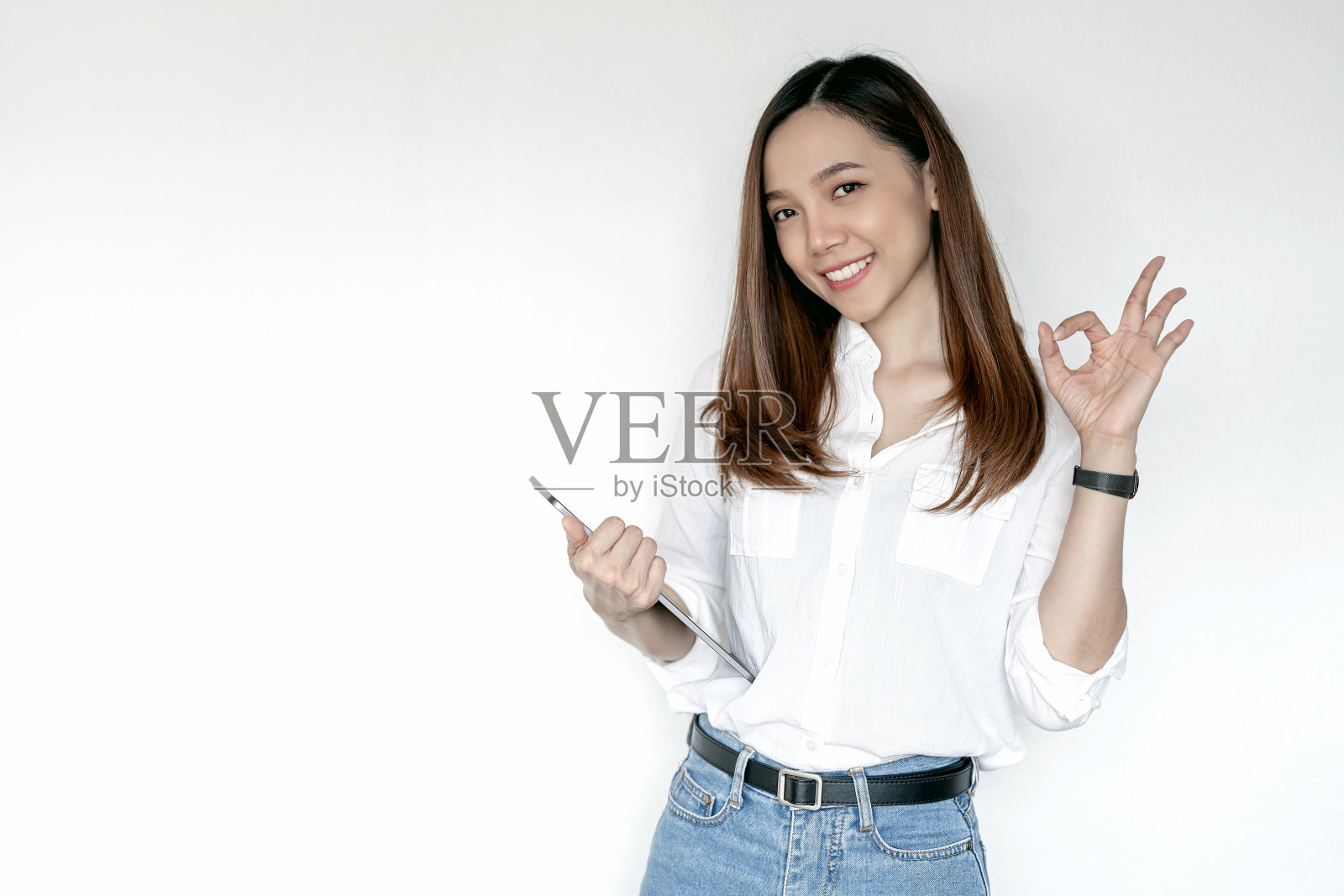 女性显示ok-sign,公司员工穿着休闲装,微笑着拿着平板电脑,站在白色背景上照片摄影图片
