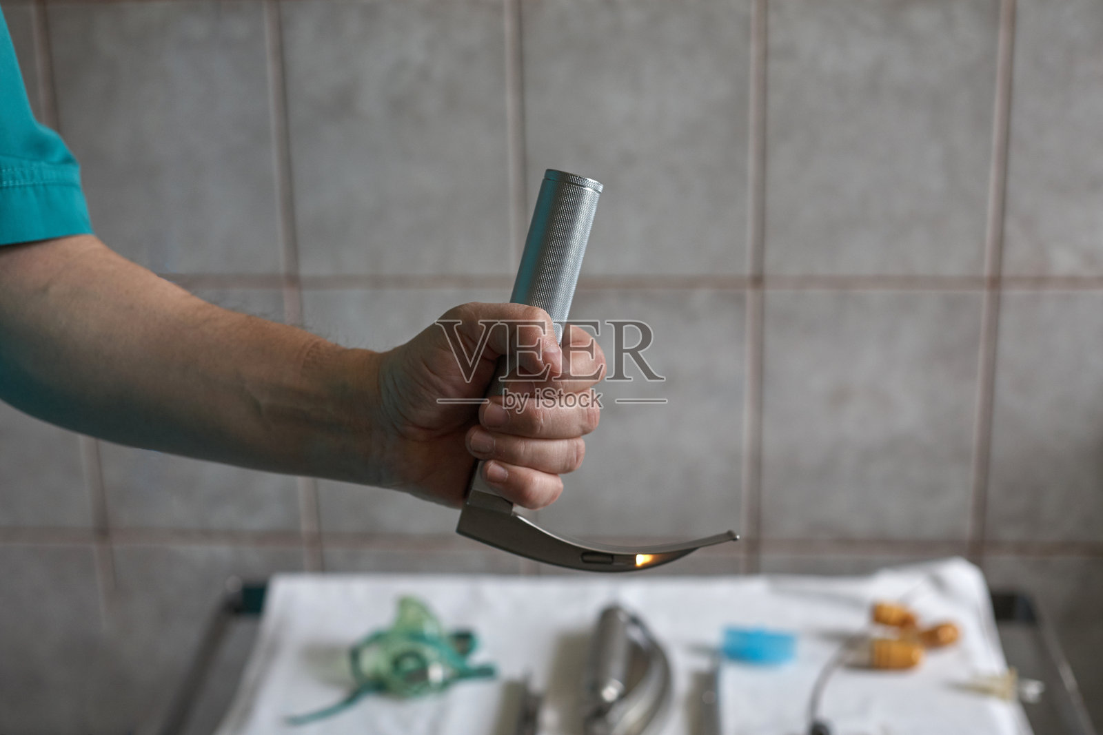 喉镜在手里。他身后是一张摆着医疗器械的桌子。照片摄影图片