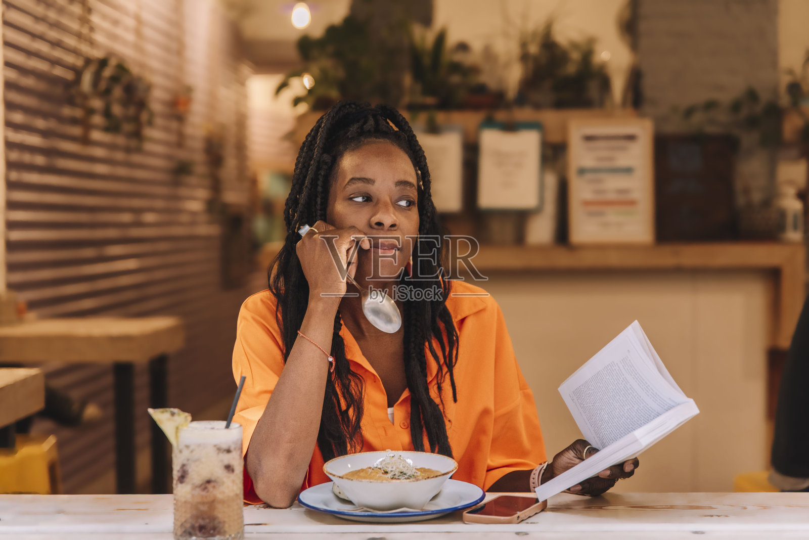 一位若有所思的非裔美国妇女一边吃饭一边拿着一本书。照片摄影图片