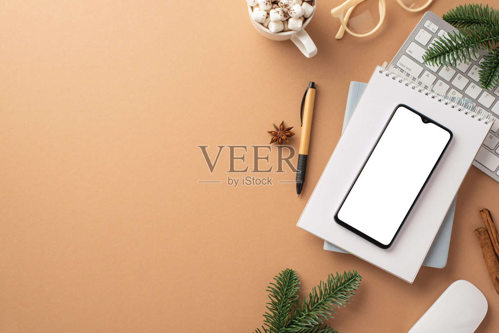 冬天的概念。智能手机提醒键盘电脑鼠标杯子的可可与棉花糖眼镜松枝肉桂棒茴芹孤立的米黄色背景与空白照片摄影图片