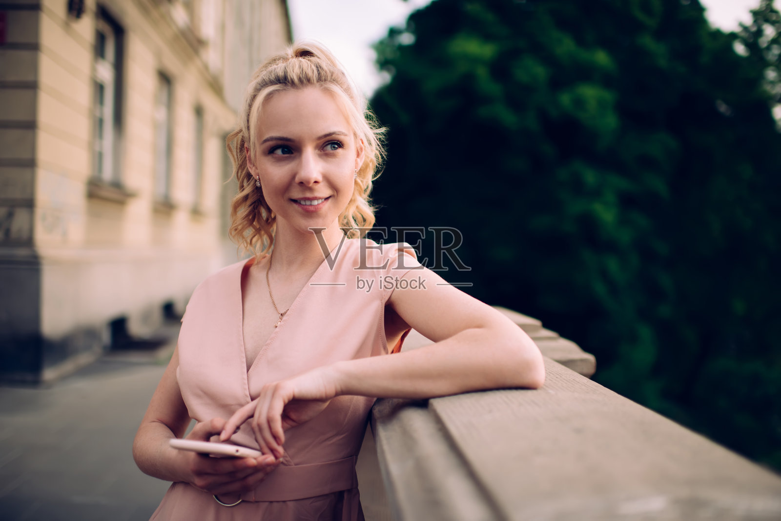 迷人的女人穿着裙子,靠在栅栏上用智能手机发短信照片摄影图片