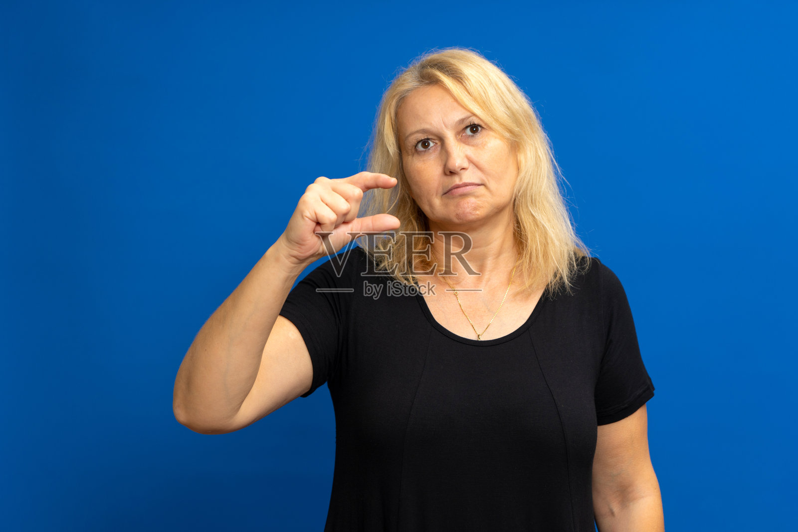 还需要一点。不满的怀疑的女人的肖像手势,不足,不满的低评级。室内工作室拍摄孤立的蓝色背景。照片摄影图片