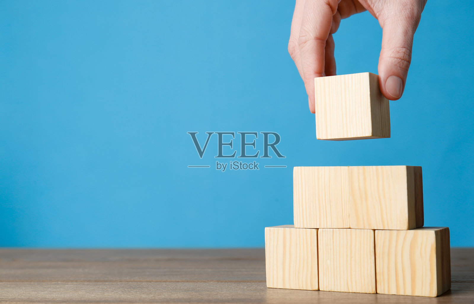 女人在浅蓝色背景的木桌上建造立方体金字塔,特写。文本空间照片摄影图片