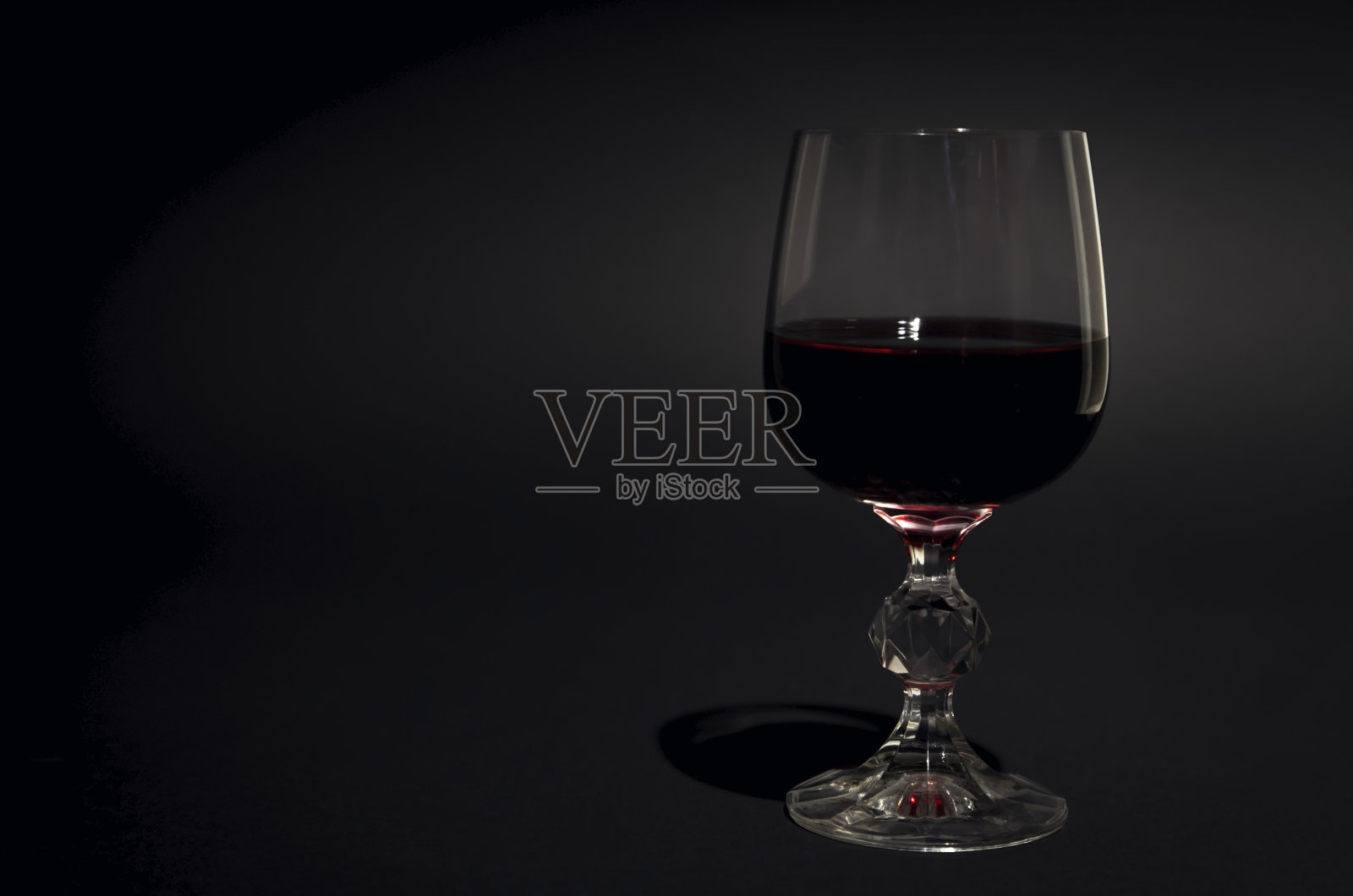 一杯红酒。红酒装在透明的玻璃杯里。黑色背景。专注于玻璃。照片摄影图片