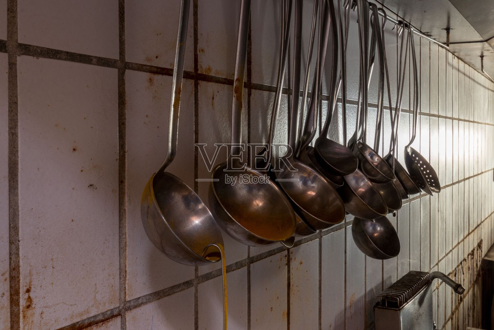 在一个令人作呕的厨房里,汤勺挂在肮脏的墙上照片摄影图片