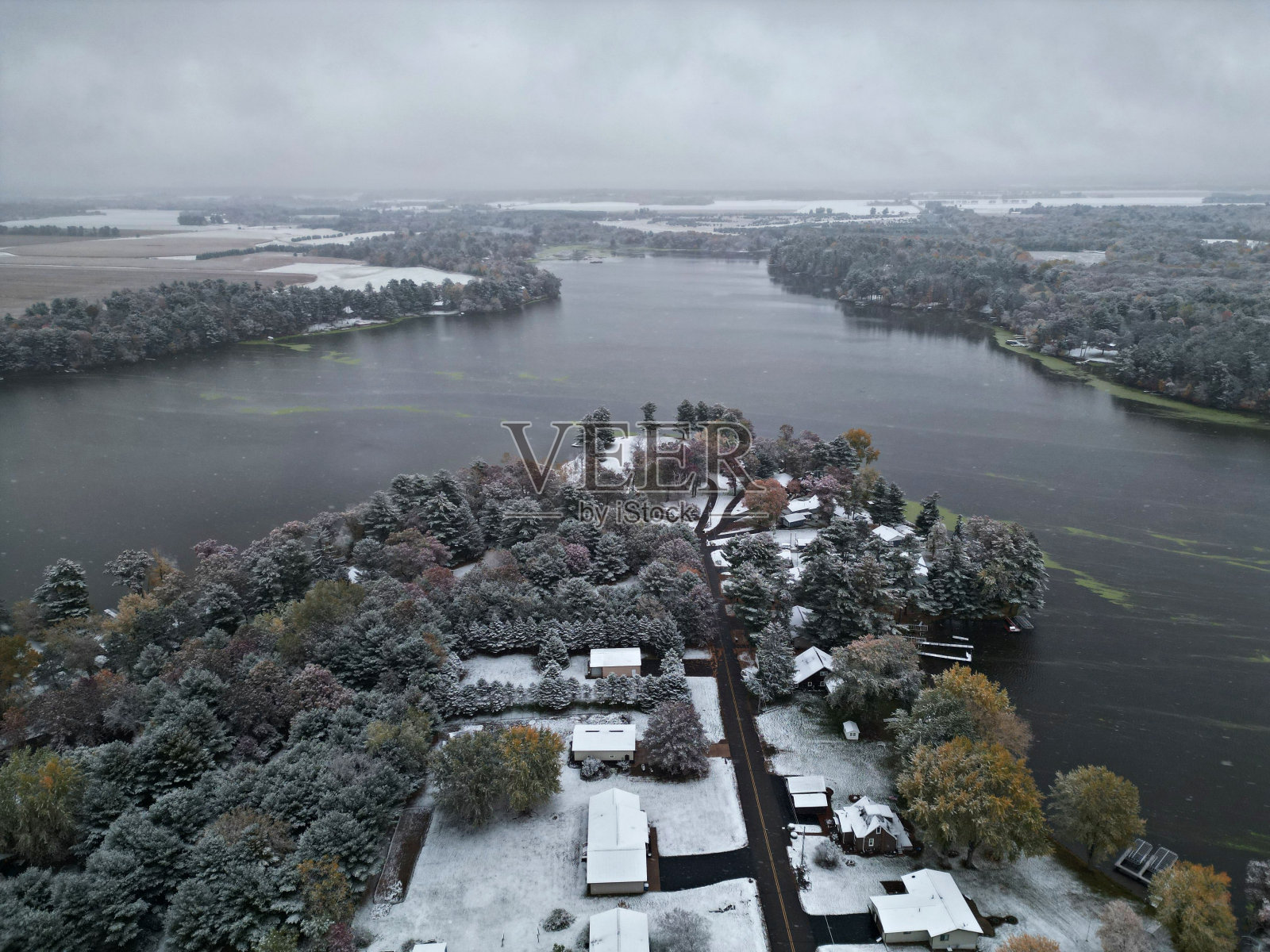 在阴天,鸟瞰湖面上被雪覆盖的房屋和树木照片摄影图片