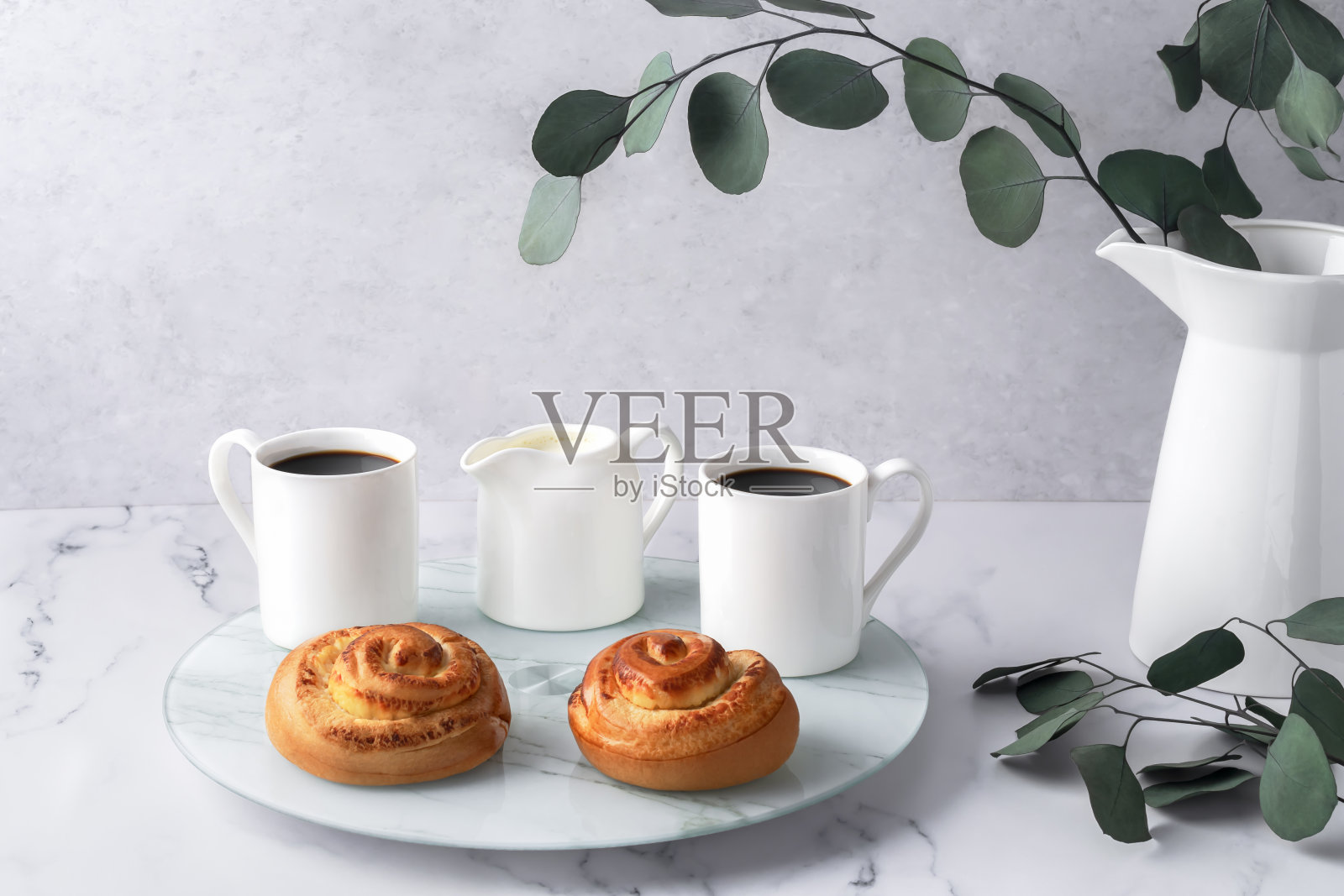 瑞典平衡生活理念,Lagom。舒适的早晨,咖啡,面包,玻璃托盘上的送奶员。白色花瓶和桉树树枝放在大理石桌子上。水平复制空间。照片摄影图片