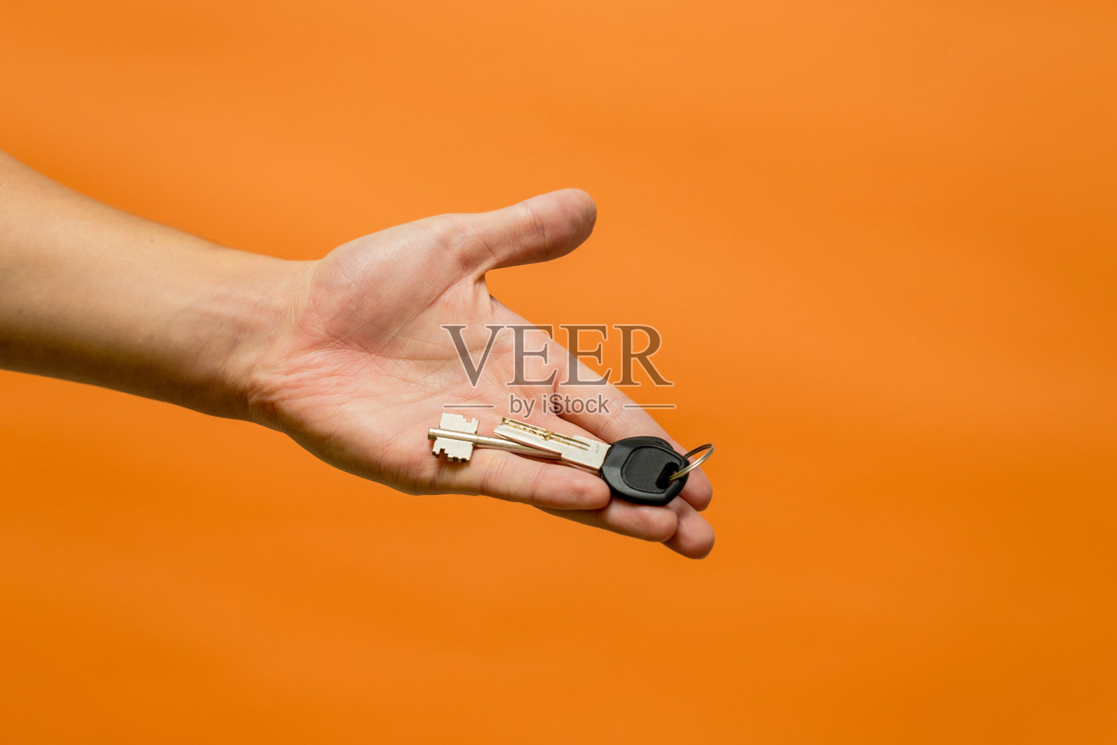 男子的手与钥匙隔离在橙色背景照片摄影图片