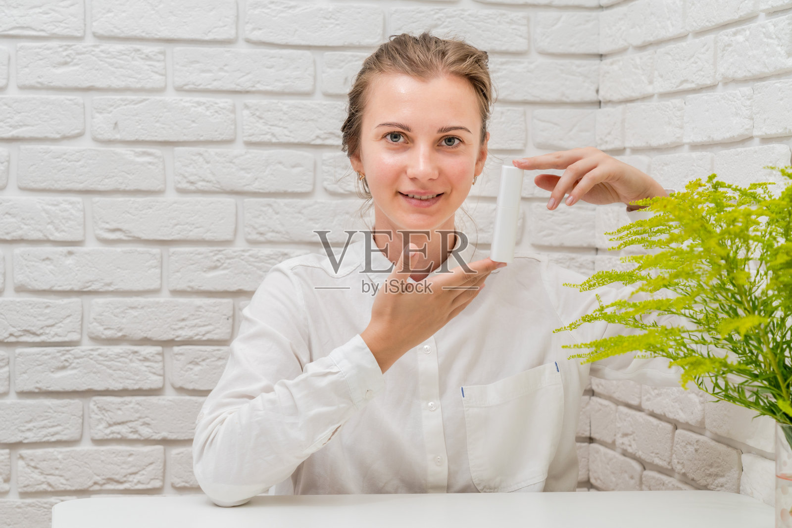 女人推荐你的化妆品与白色砖墙背景。化妆品,美容和水疗或医药概念照片摄影图片