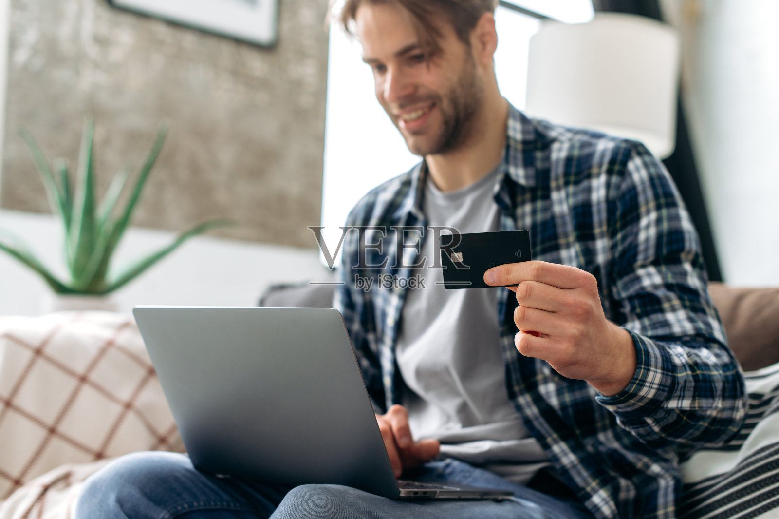 积极分散的白人男子在网上购物,使用笔记本电脑和信用卡,享受网上购物,在网上商店购买商品,坐在舒适的客厅进行远程支付照片摄影图片